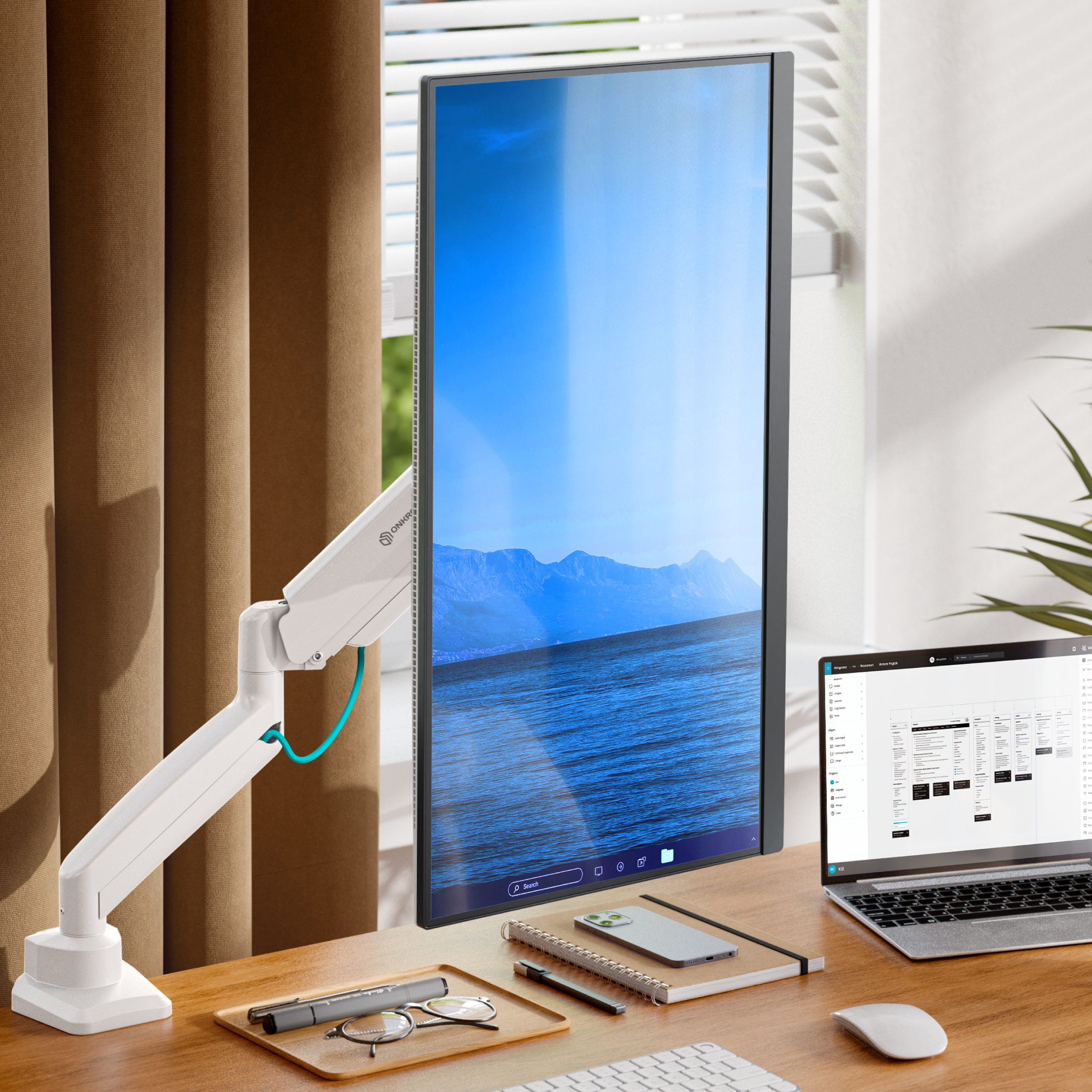 Ein vertikaler Monitor mit Landschaftstapete steht auf einem Schreibtisch mit Laptop, Telefon, Notizbuch, Brille und Stift.
