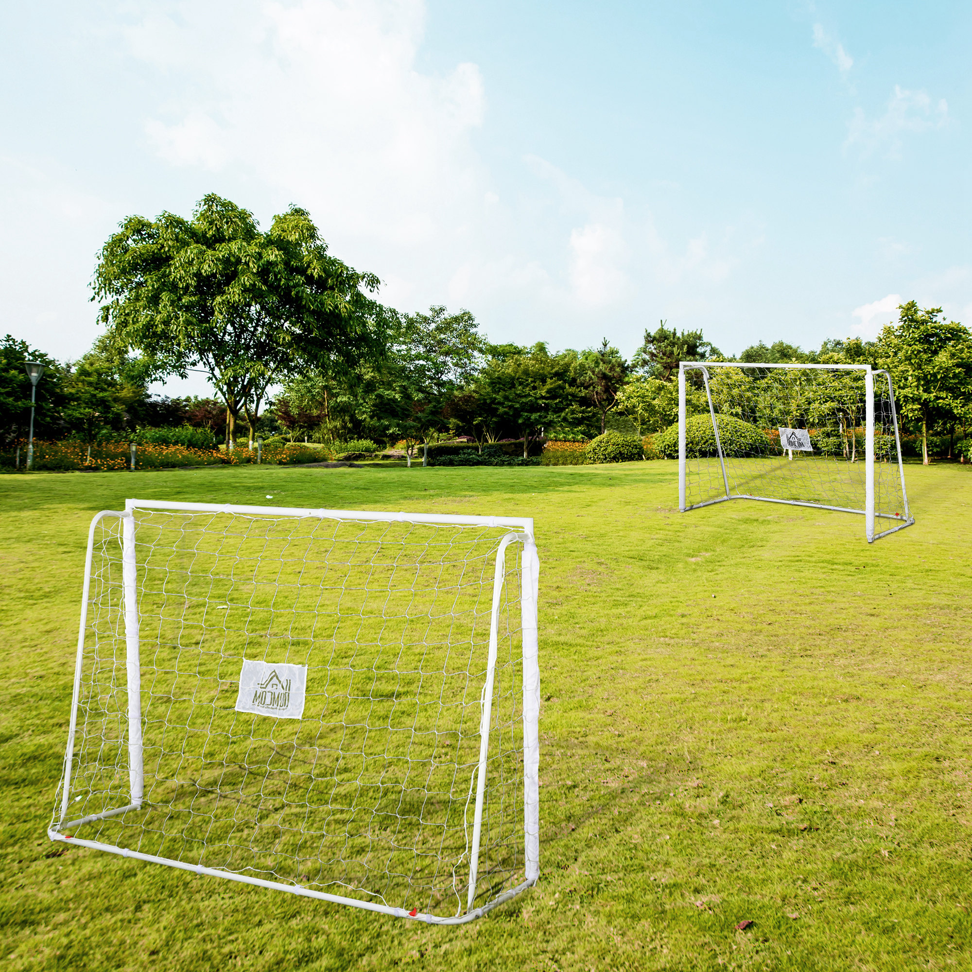 Dos porterías de fútbol blancas sobre césped verde con árboles al fondo.