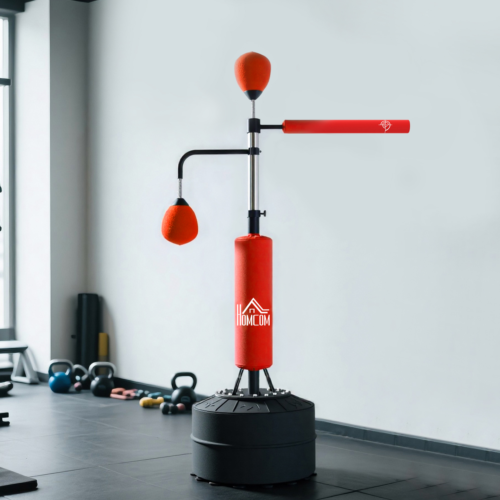Un saco de boxeo rojo con base alta se encuentra en un gimnasio. Hay pesas y kettlebells cerca.