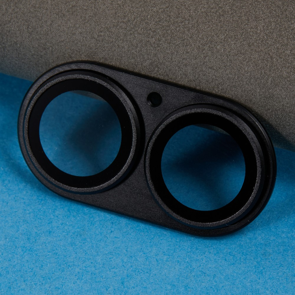 Un cadre d'objectif noir avec deux ouvertures circulaires sur fond bleu et gris.