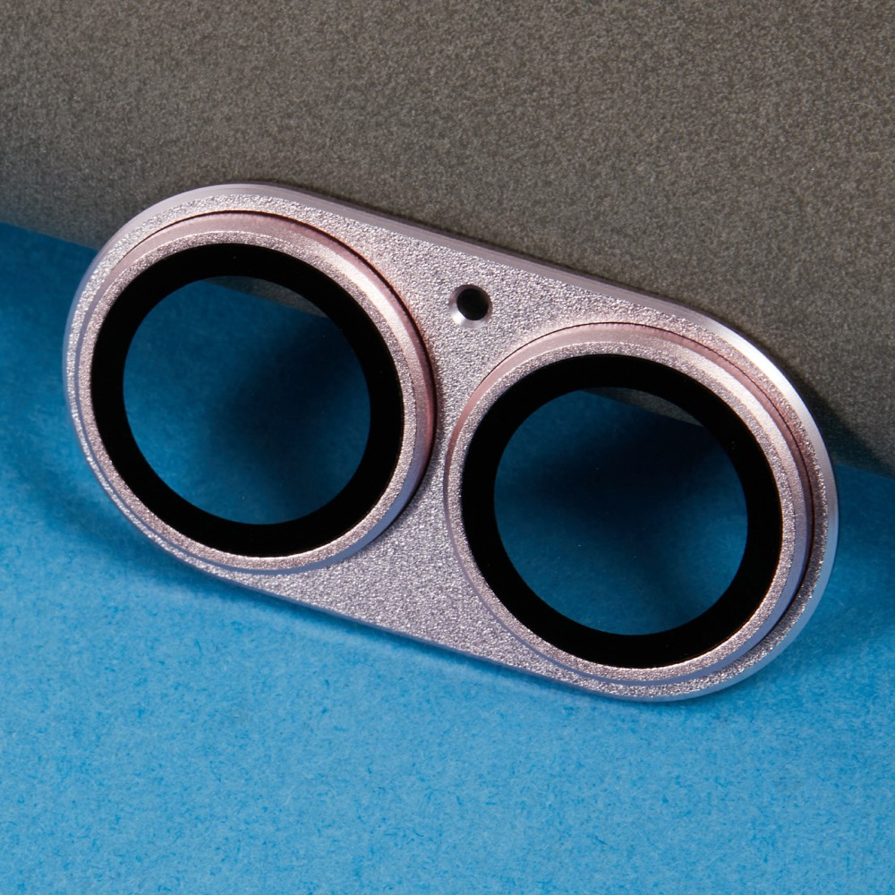 Cache objectif double caméra or rose avec anneaux noirs sur fond bleu et gris.