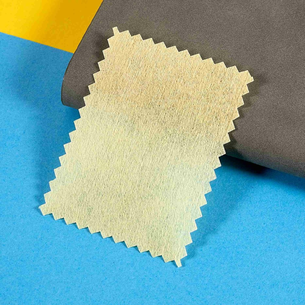 Un échantillon de tissu jaune pâle à bords en zigzag sur fond bleu et jaune.