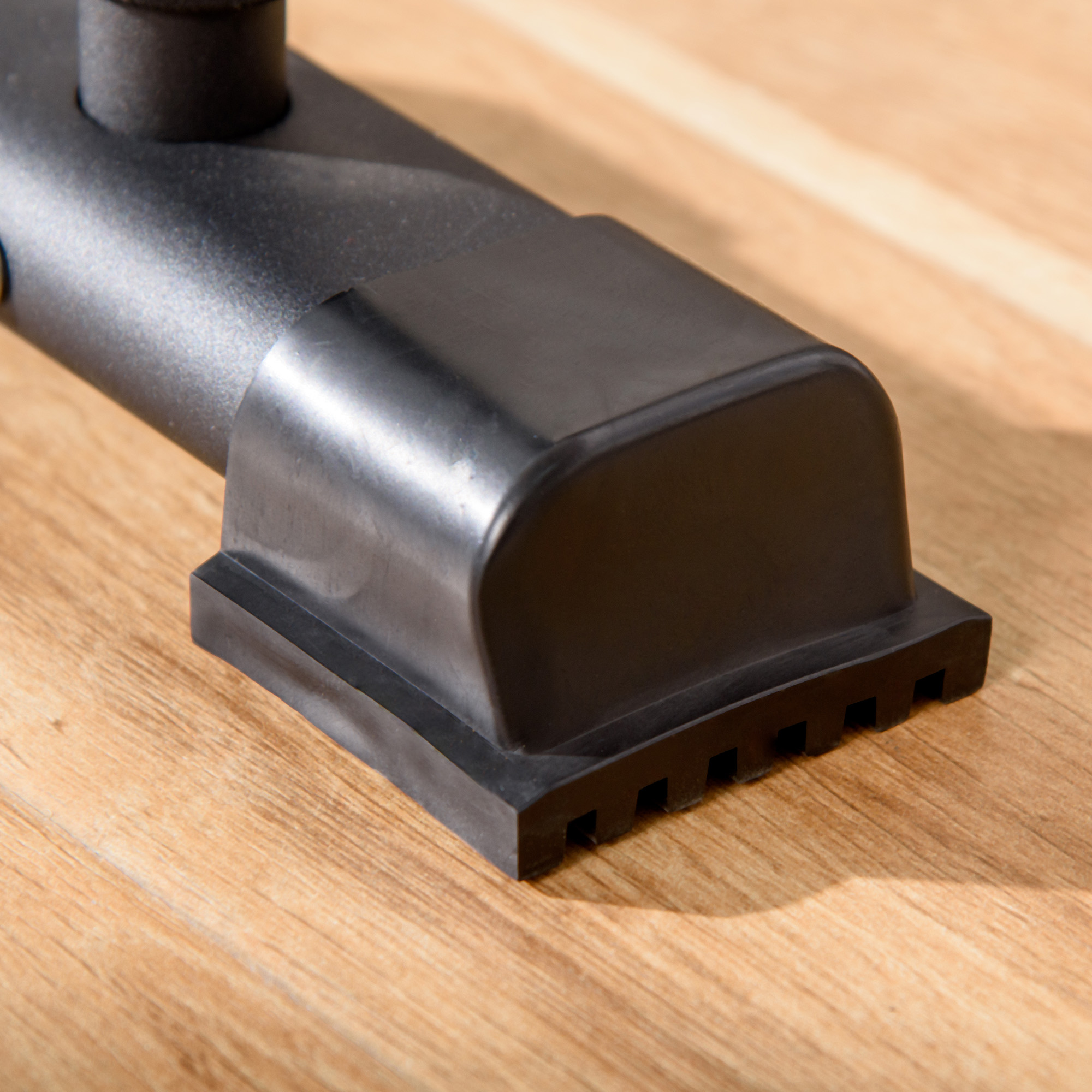 Accesorio de goma negro con ranuras sobre una superficie de madera.