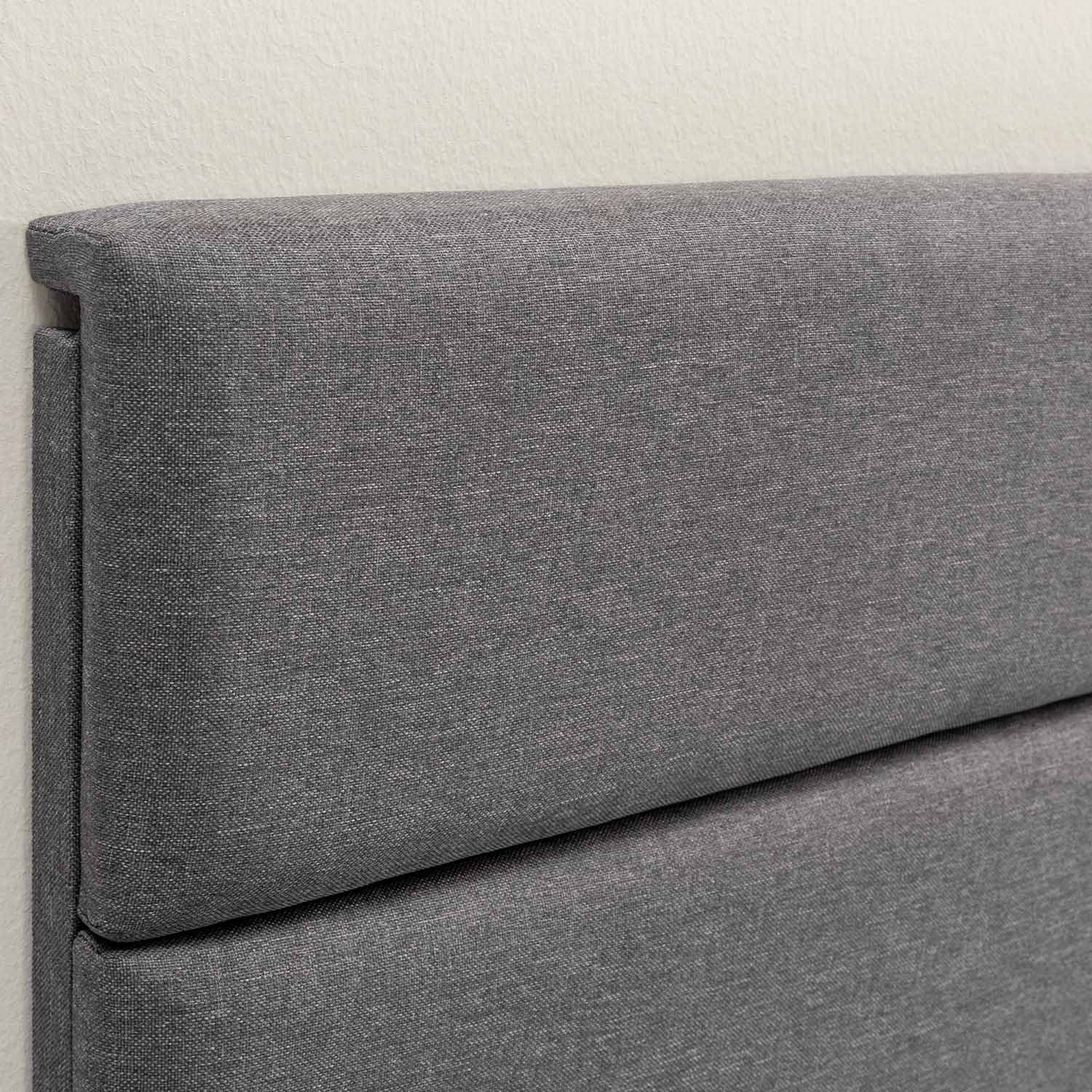 Cabecero de tela gris con textura, fijado a una pared color crema.