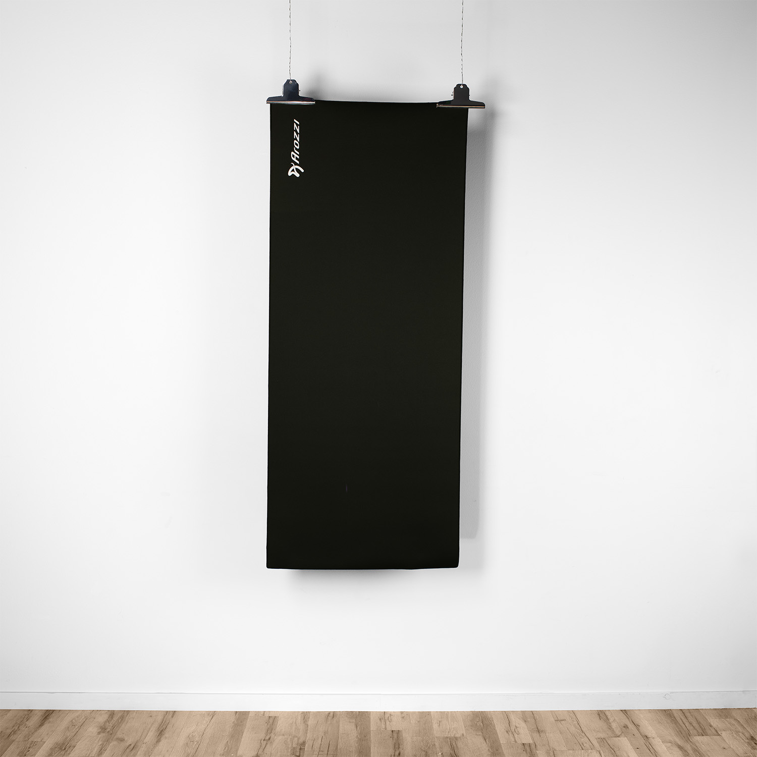 Un panno nero pende da un muro bianco, tenuto da una clip su un filo. Logo visibile.