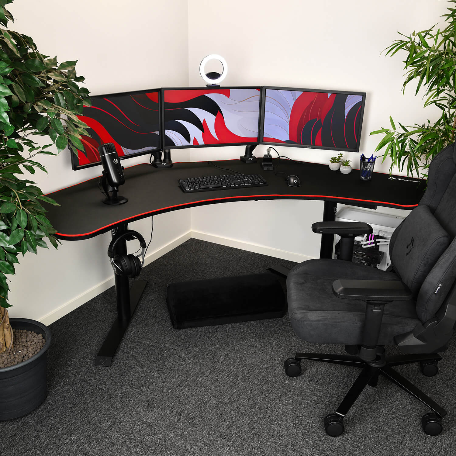 Una postazione gaming angolare con tripli monitor, microfono, tastiera, mouse e sedia nera.