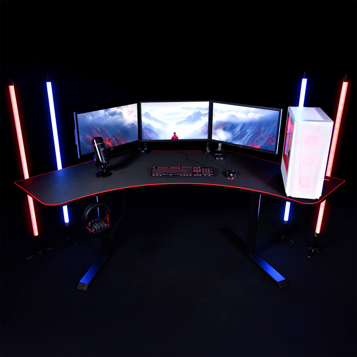 Una scrivania da gaming con tre monitor, tastiera, mouse, microfono e PC. Luci rosse e blu.