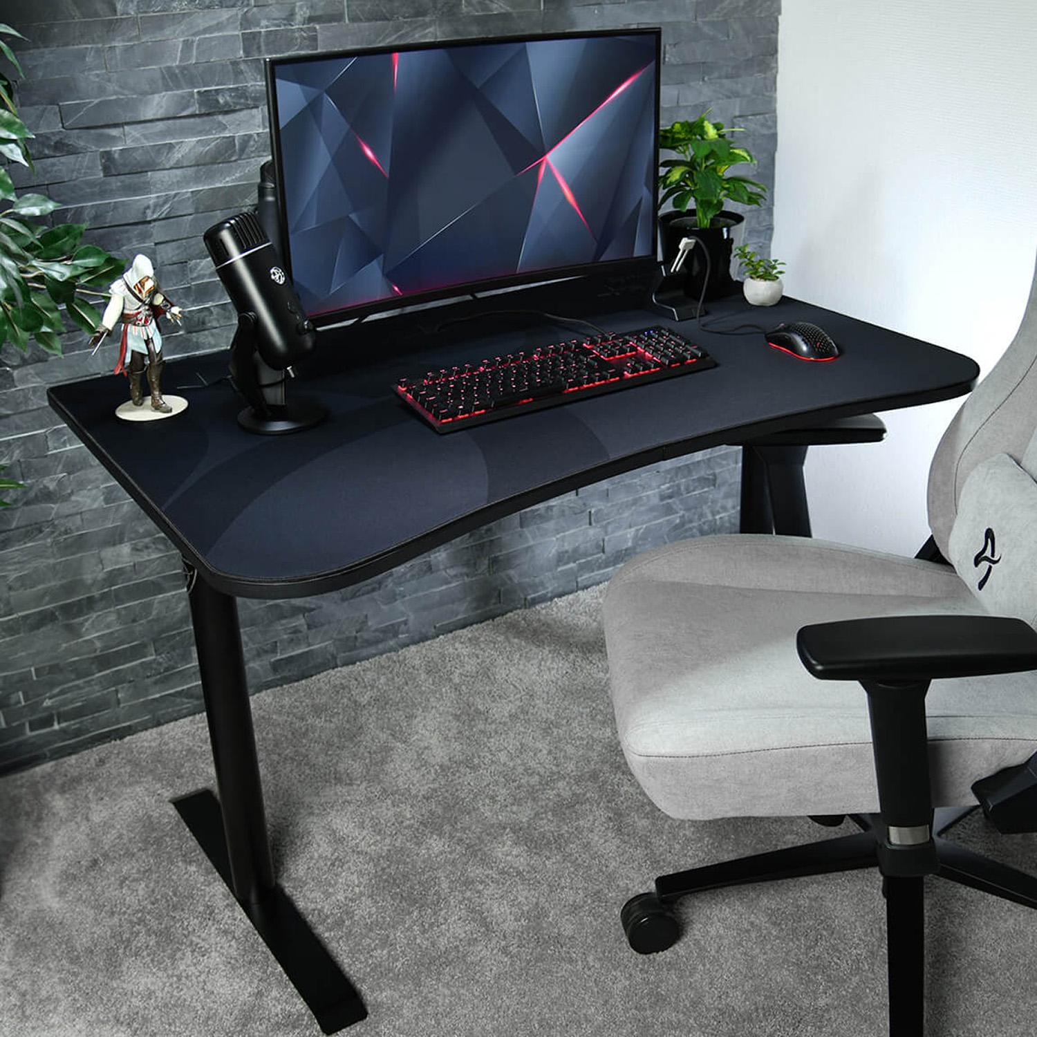 Scrivania gaming con monitor, tastiera, mouse, microfono e statuetta. Sedia grigia.