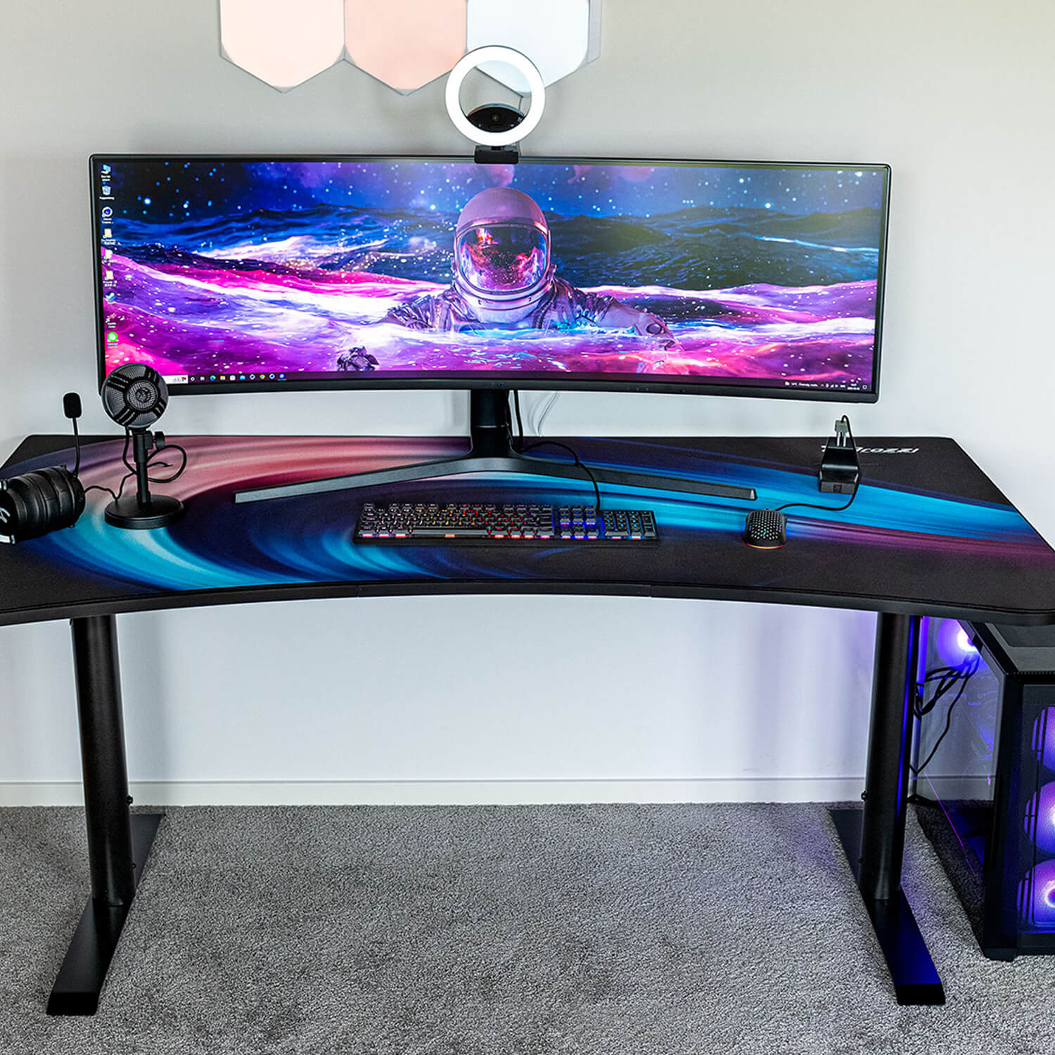 A desk with a large curved monitor, keyboard, mouse, microphone, and headphones.