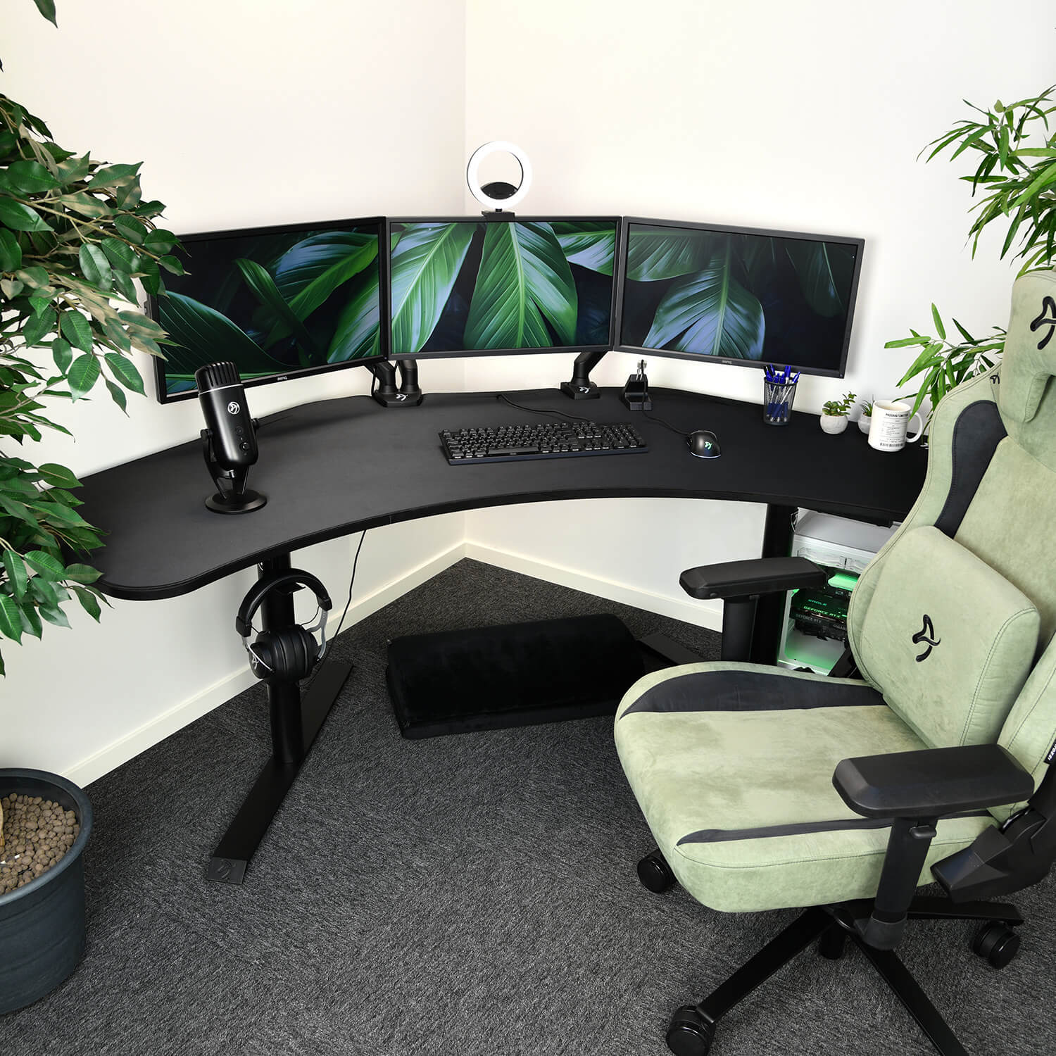 Una moderna postazione da gaming con tre monitor, una scrivania nera e una sedia verde chiaro.