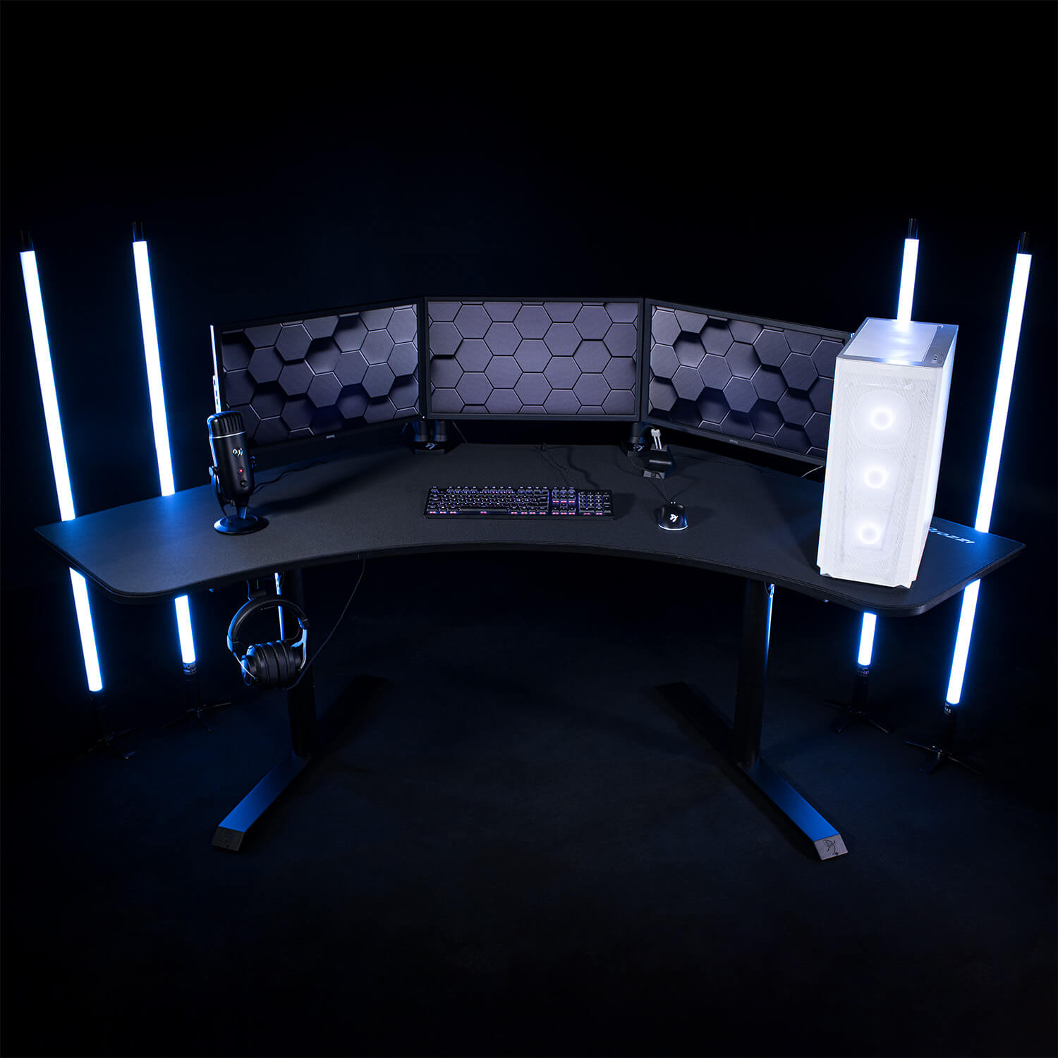Una scrivania da gaming con tre monitor, microfono, tastiera, mouse e PC bianco.