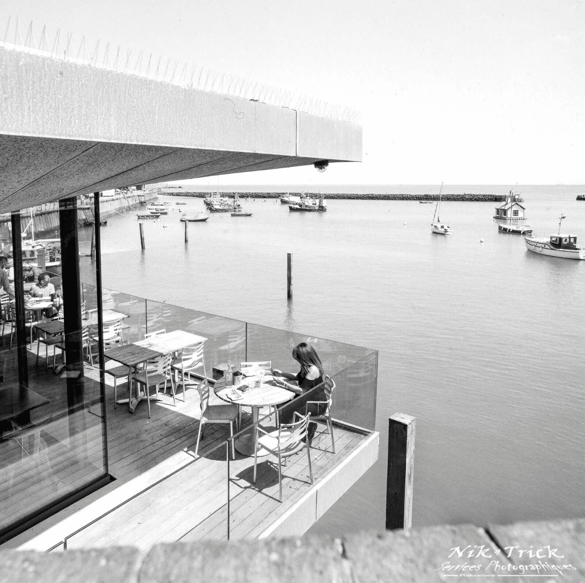 Una mujer se sienta en una mesa en un balcón con vistas a un puerto con muchos barcos.