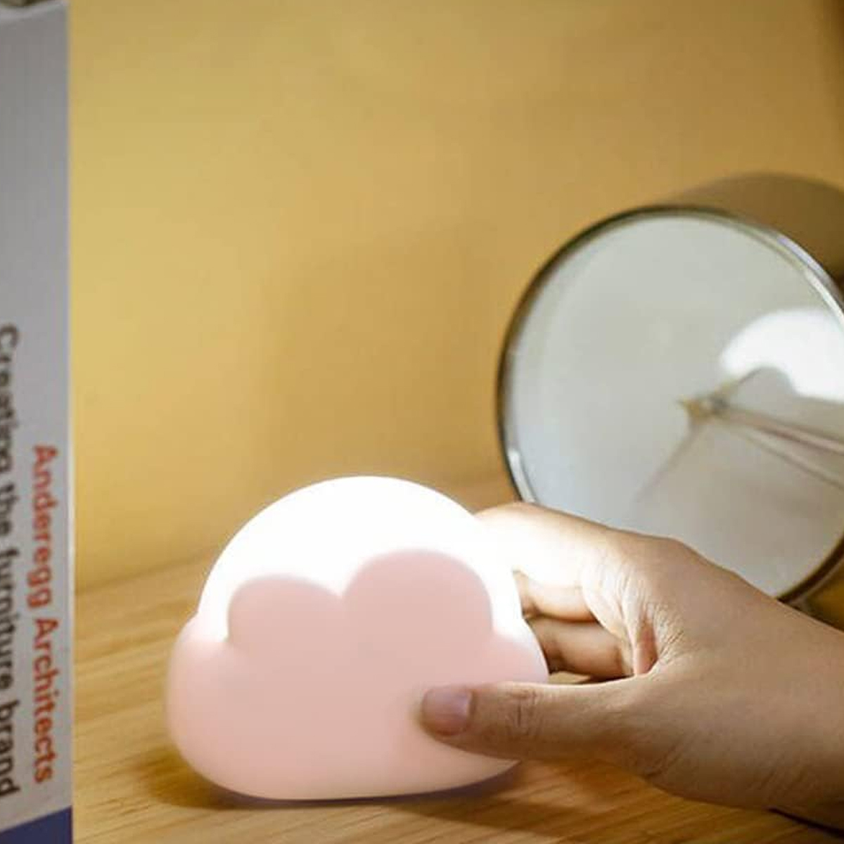 Eine Hand hält ein leuchtendes rosa wolkenförmiges Nachtlicht auf einer Holzoberfläche.