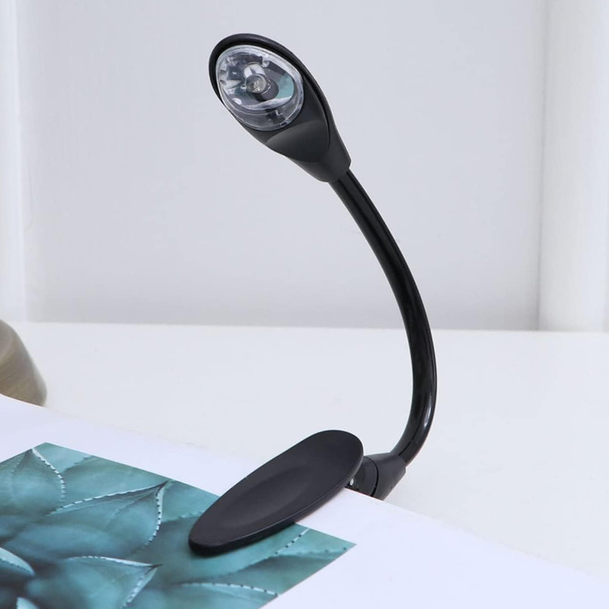 Ein schwarzes Klemmbuchlicht mit flexiblem Hals und LED-Lampe, das auf einem Buch befestigt ist.