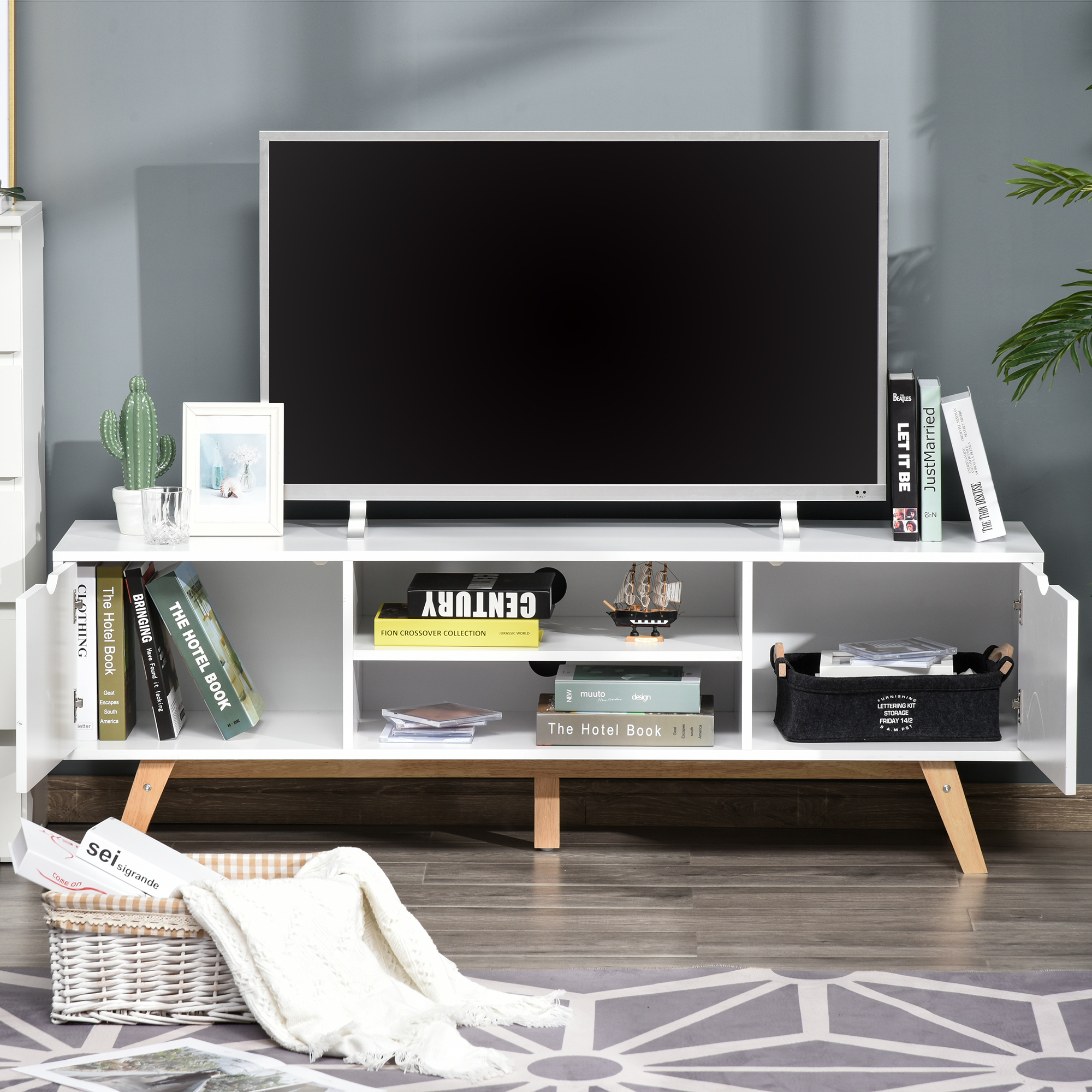 Un moderno mueble de TV blanco con un televisor, libros y plantas.