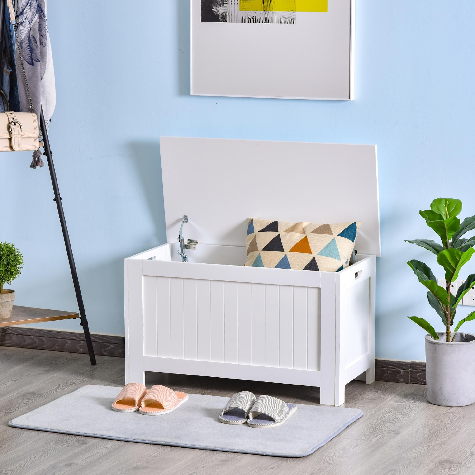 Un banco de almacenamiento blanco con cojín, planta y ropa cerca.