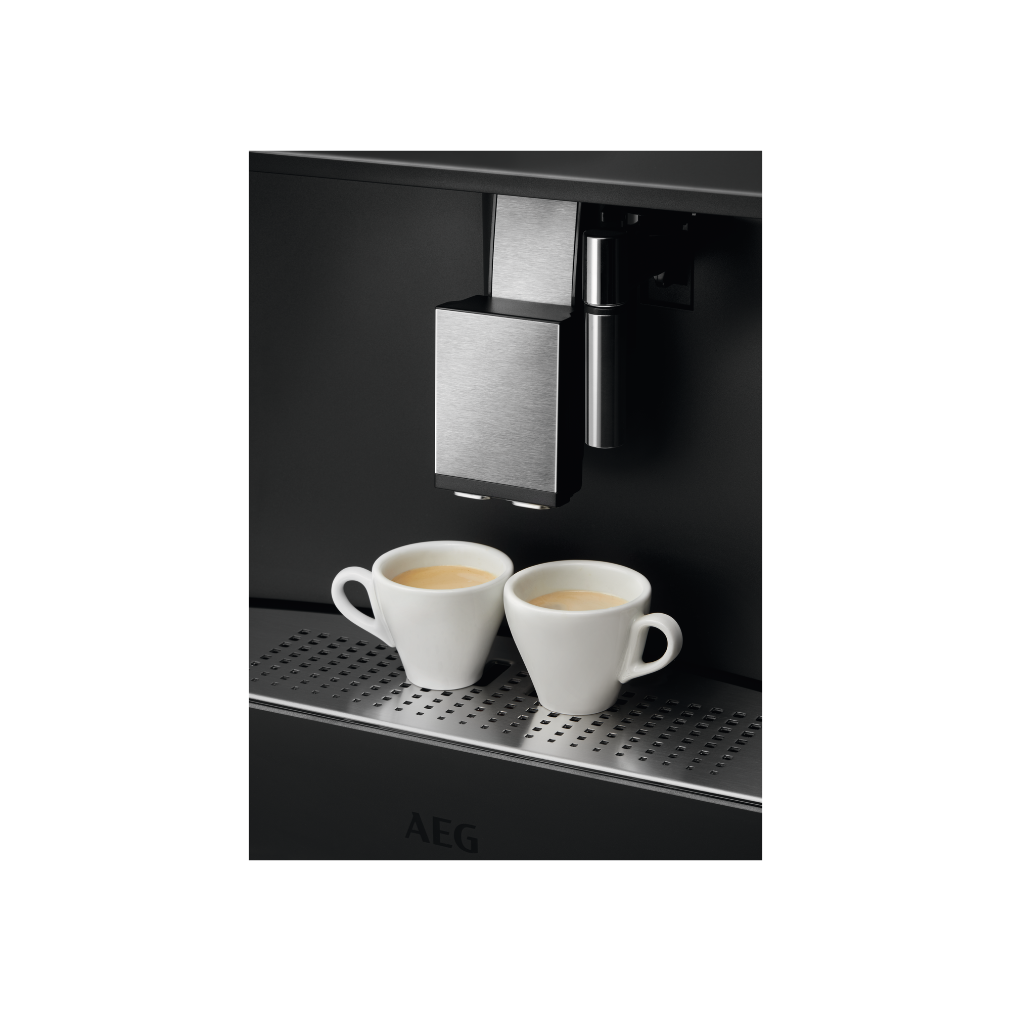 Dos tazas de espresso blancas en la bandeja de goteo de una cafetera.