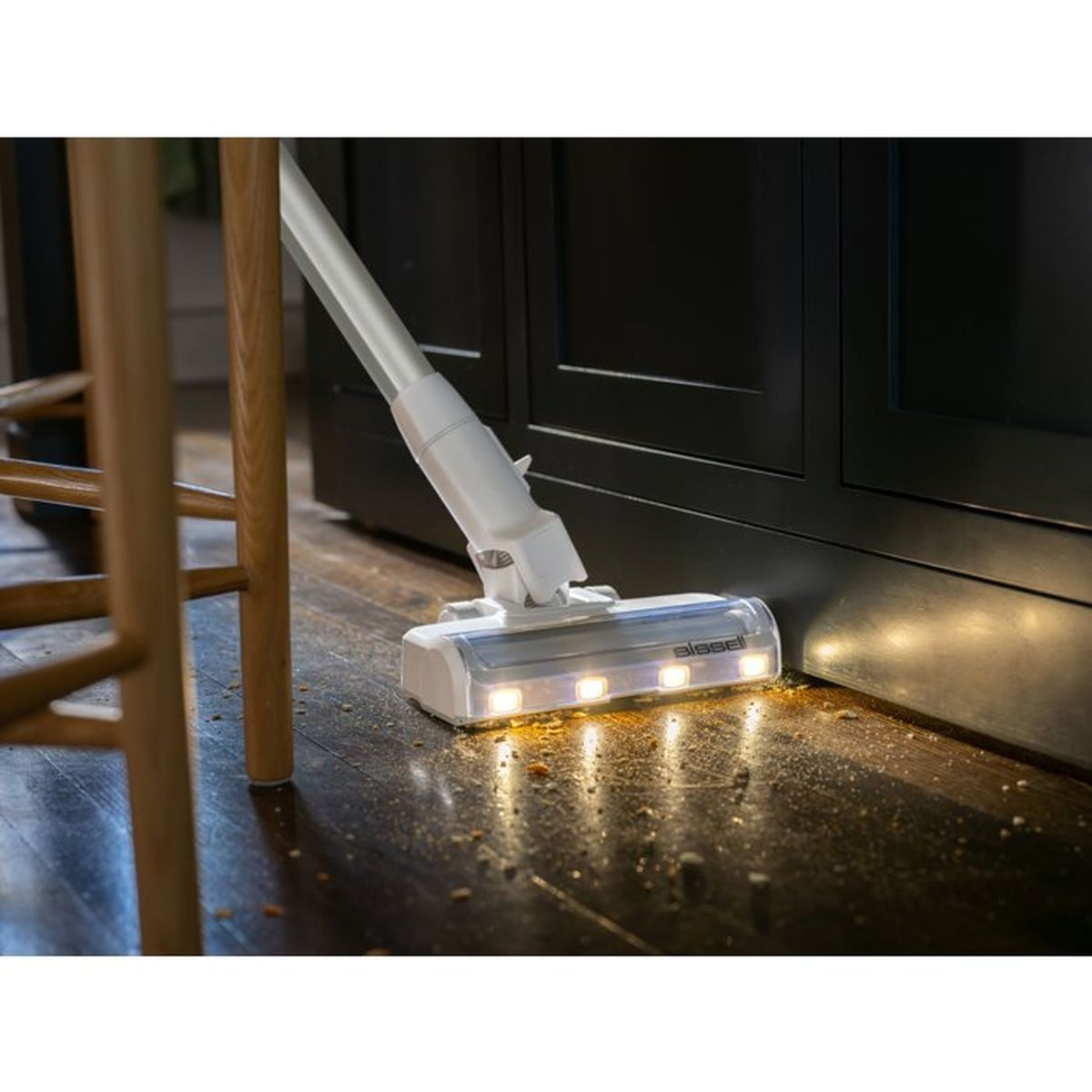 A white vacuum cleaner head with lights cleans a dirty wooden floor.
