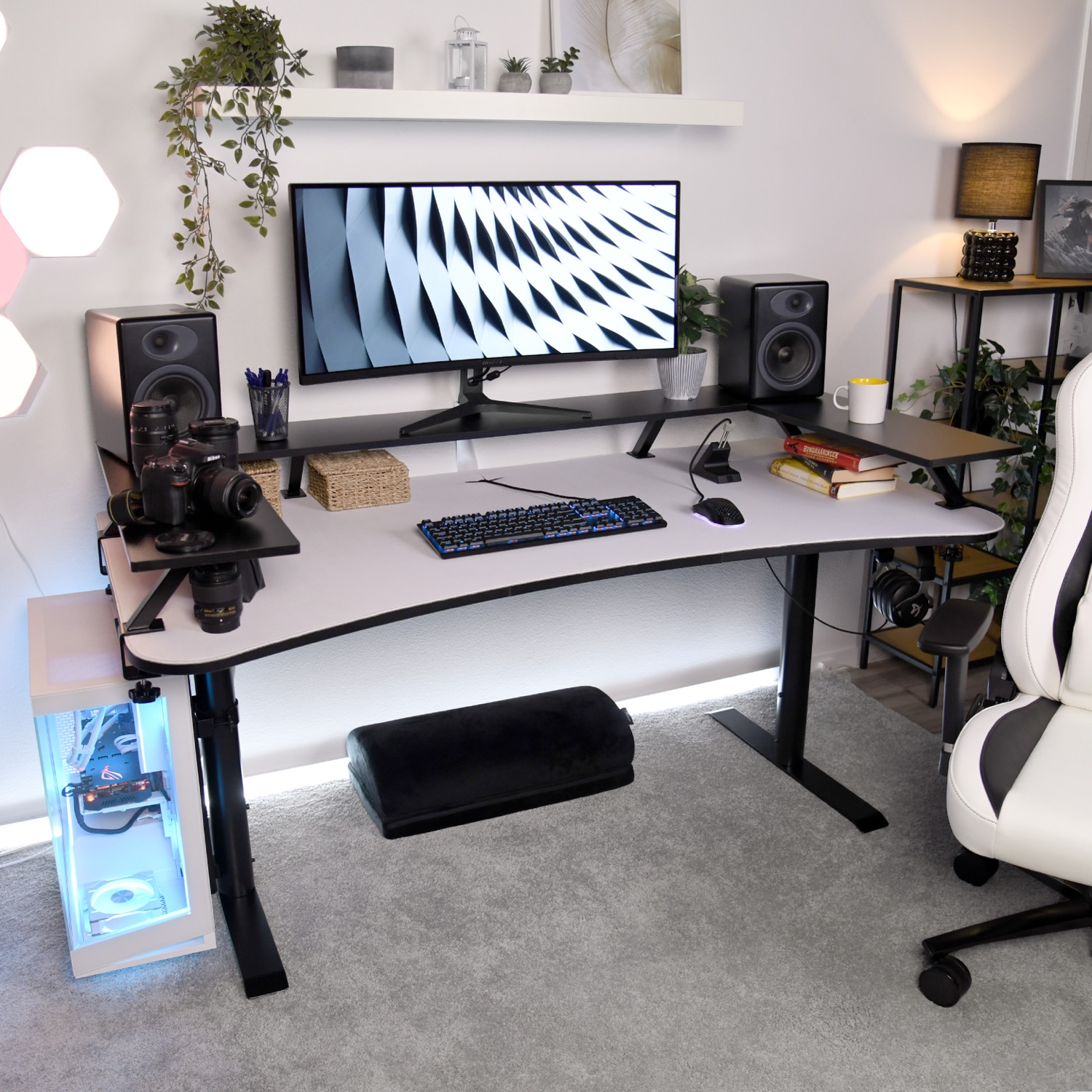 Een moderne bureauopstelling met computer, camera, luidsprekers en een witte gamestoel.