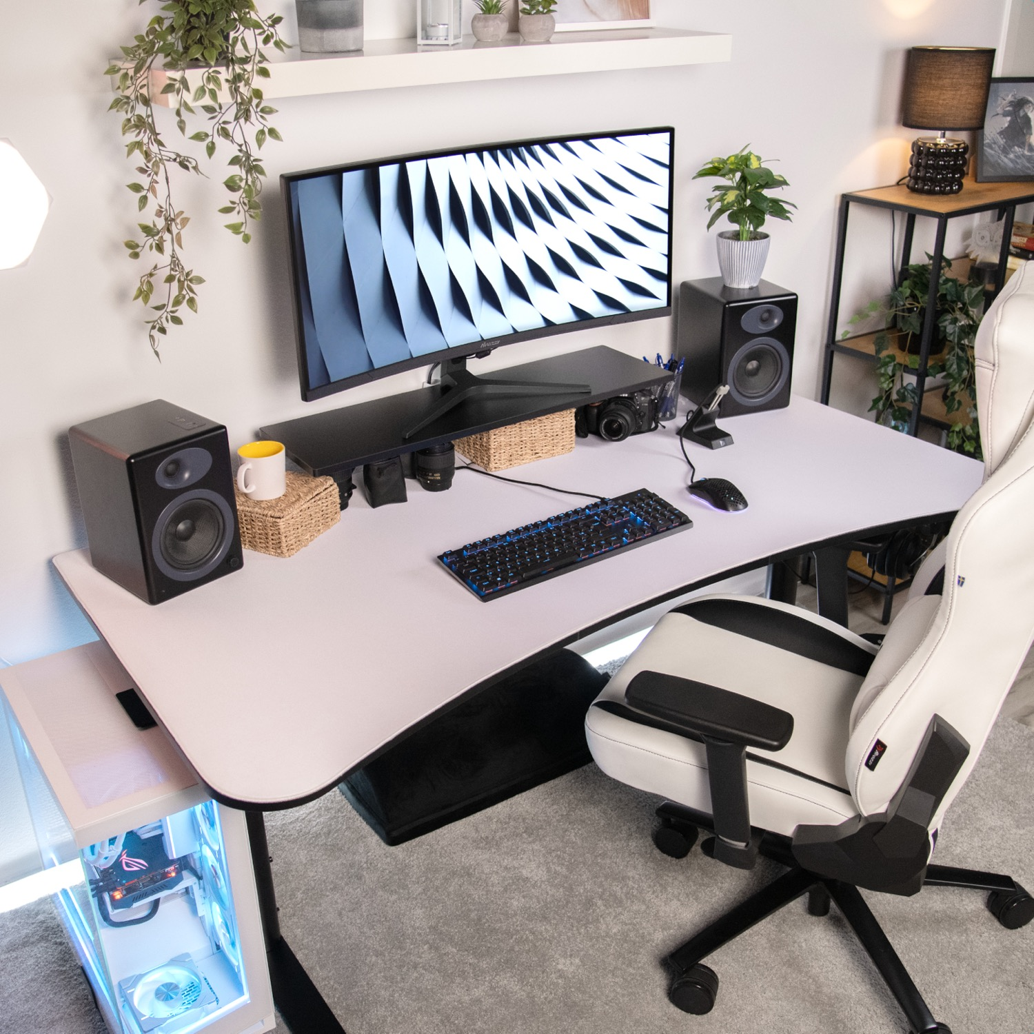 Een wit bureau met monitor, luidsprekers, toetsenbord, muis en een witte gamestoel.