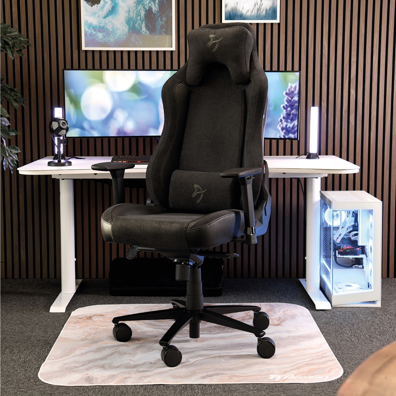 Sedia da gaming nera su tappeto effetto marmo davanti a scrivania bianca con monitor.