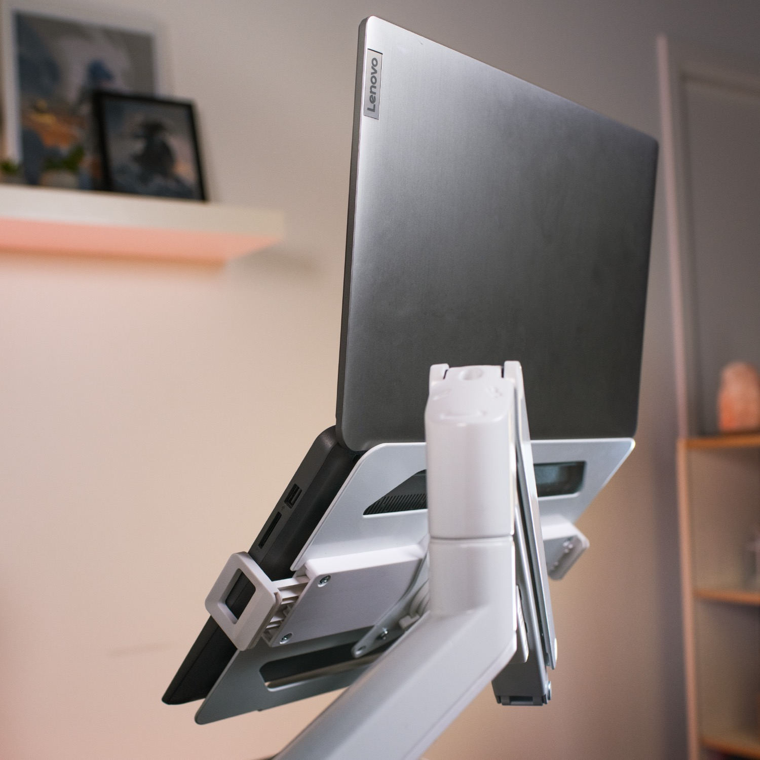 Een laptop op een witte standaard, met schilderijen op de achtergrond.