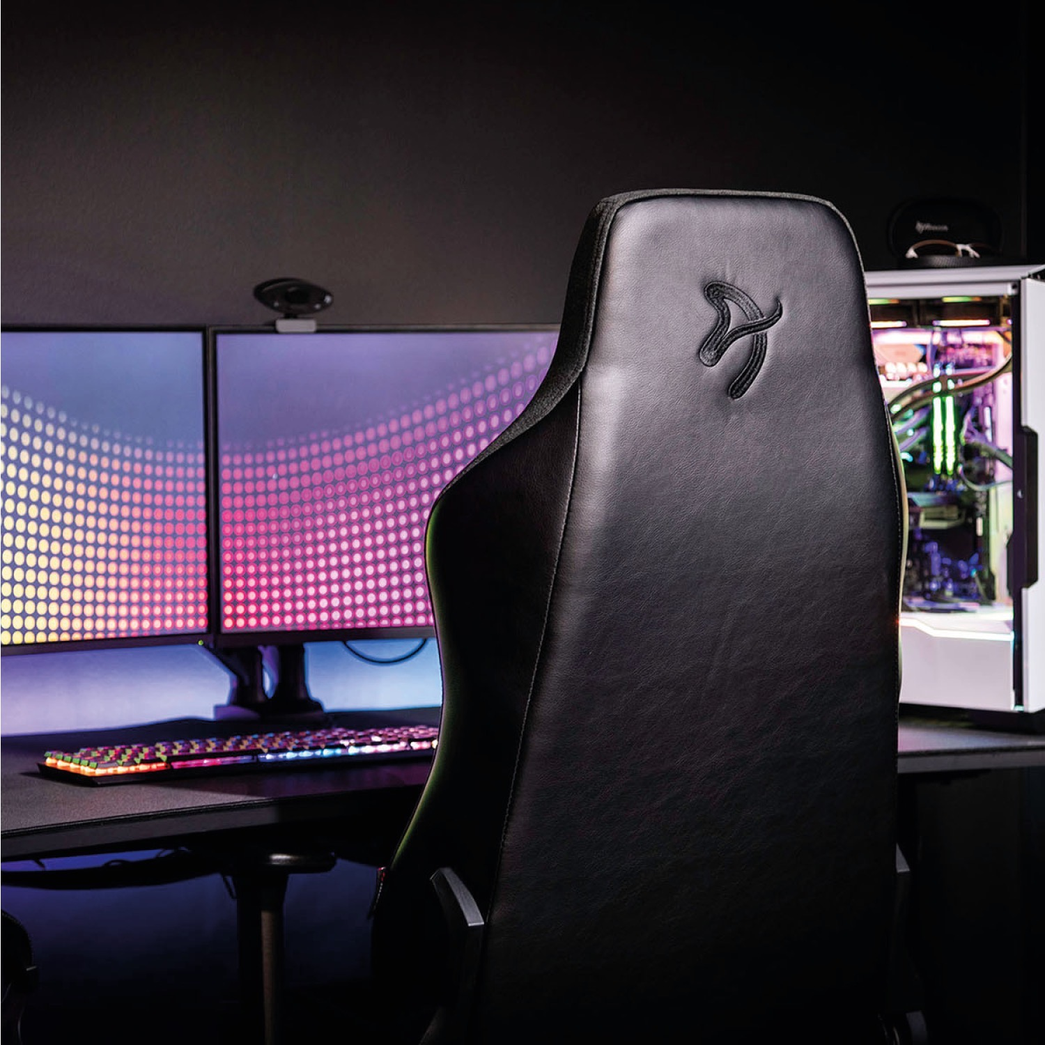 Sedia da gaming nera con logo, due monitor, tastiera e PC, il tutto illuminato da RGB.