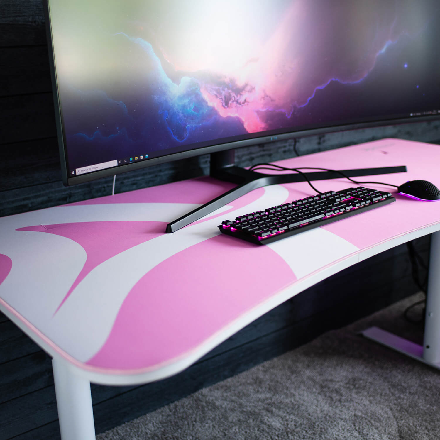 Una scrivania rosa e bianca con tastiera, mouse e monitor neri.