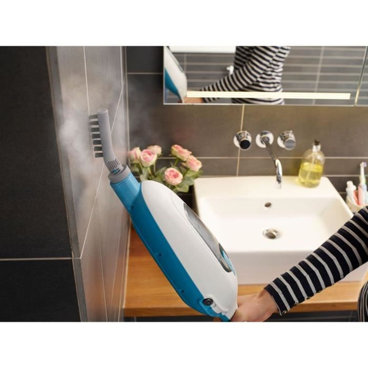 Un limpiador a vapor con accesorio de cepillo limpia una pared oscura de azulejos junto a un lavabo.