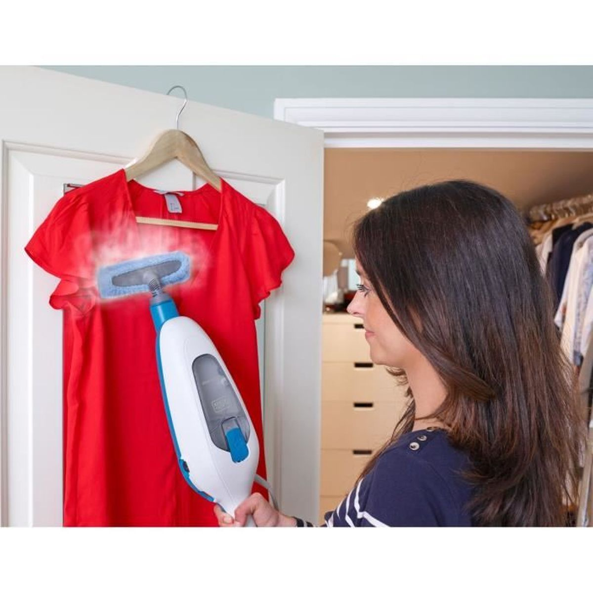 Una mujer plancha una camisa roja colgada en una puerta con un vaporizador.