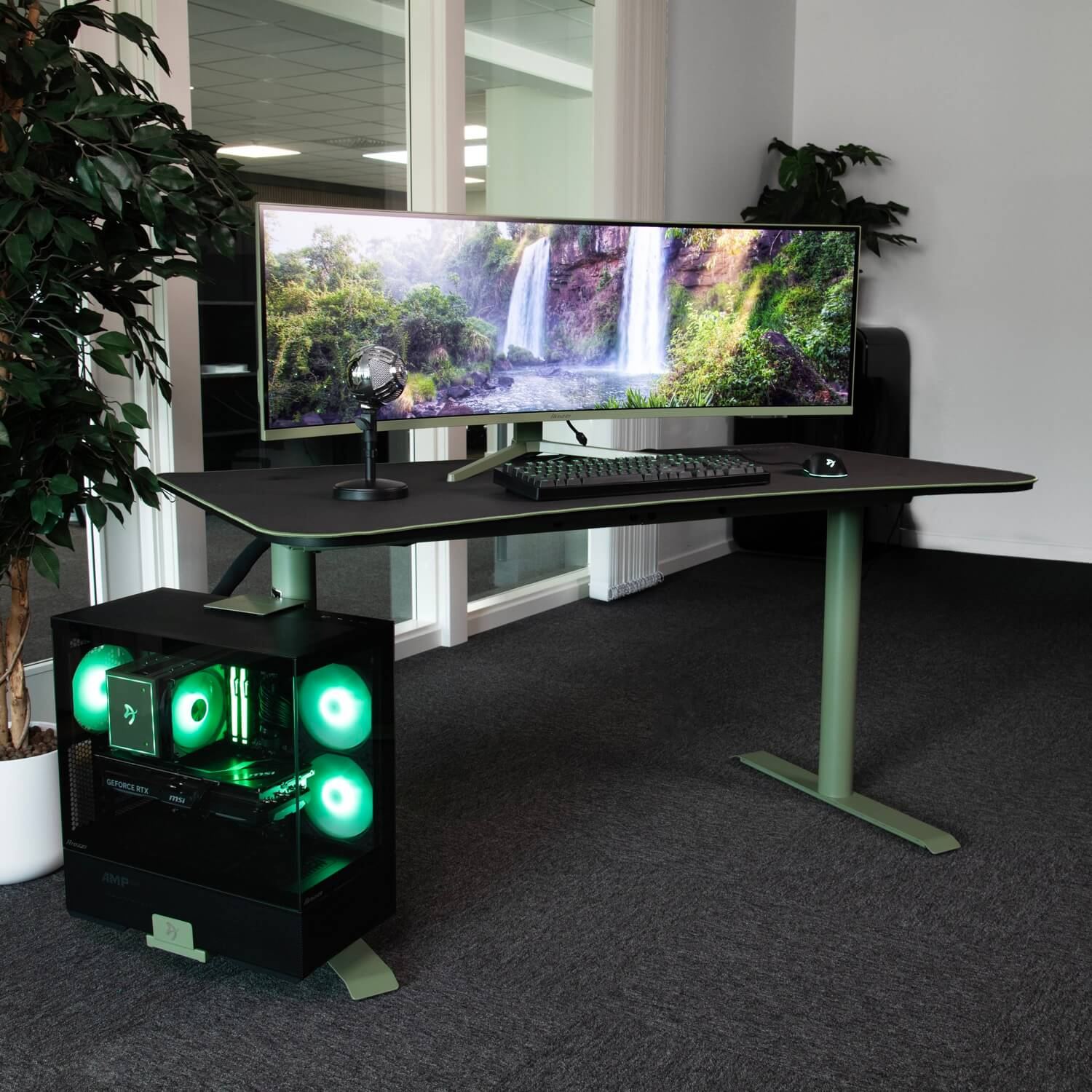 Una scrivania con un ampio monitor che mostra una cascata. Accanto, un PC con illuminazione verde.