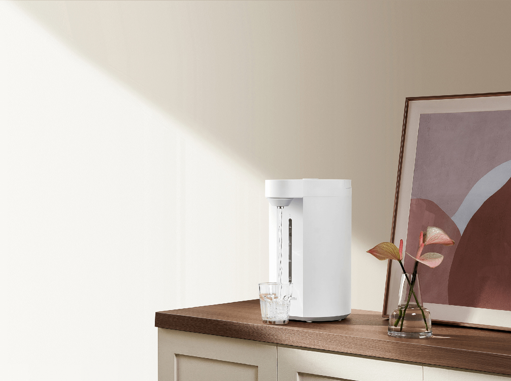 A white water dispenser fills a glass on a wooden cabinet. Beside it, a vase with flowers.