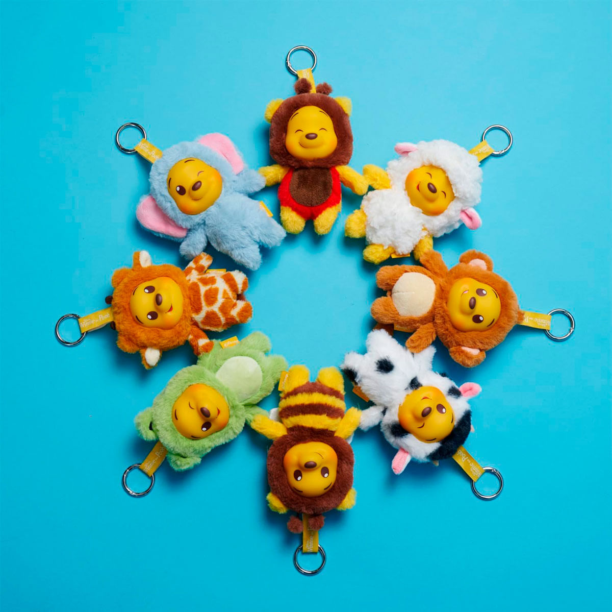 Un cercle de peluches Winnie l'Ourson déguisés en animaux sur fond bleu.