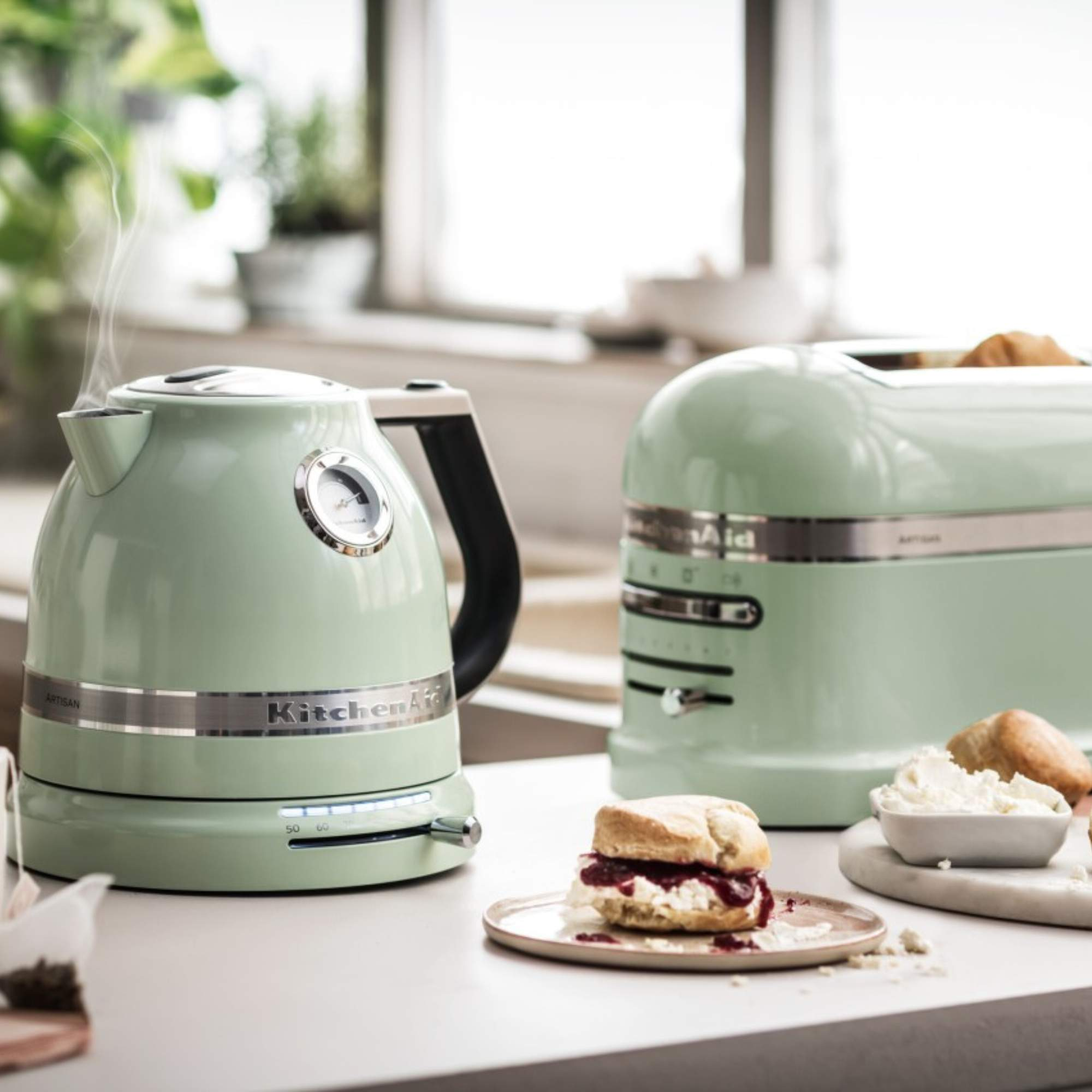 Grüner Wasserkocher mit Thermometer, Toaster und Scone mit Marmelade.