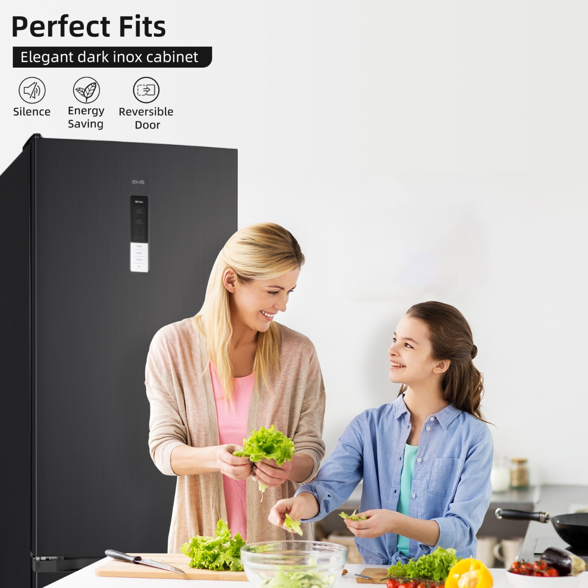 A woman and girl prepare salad in front of a black refrigerator.