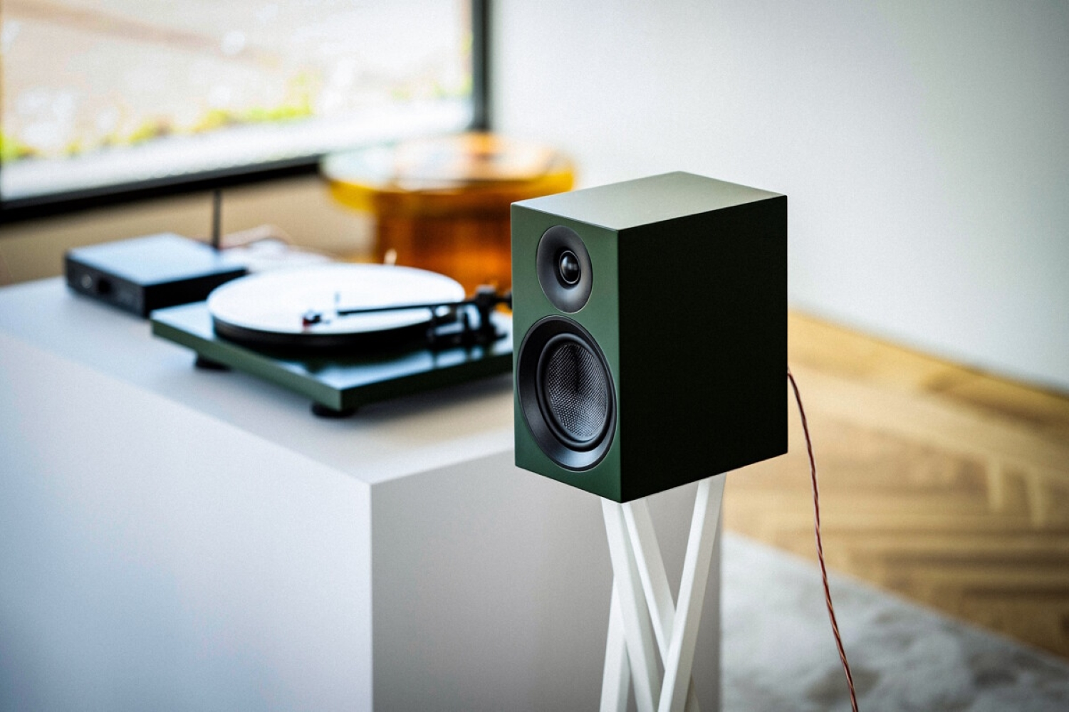 Ciemnozielony głośnik stoi na białym stojaku obok gramofonu.