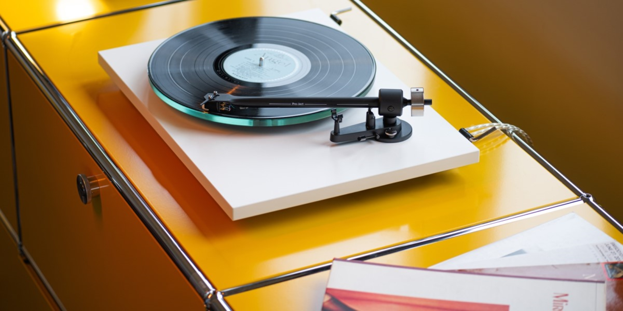 Gramofon z czarną płytą winylową na żółtym meblu.