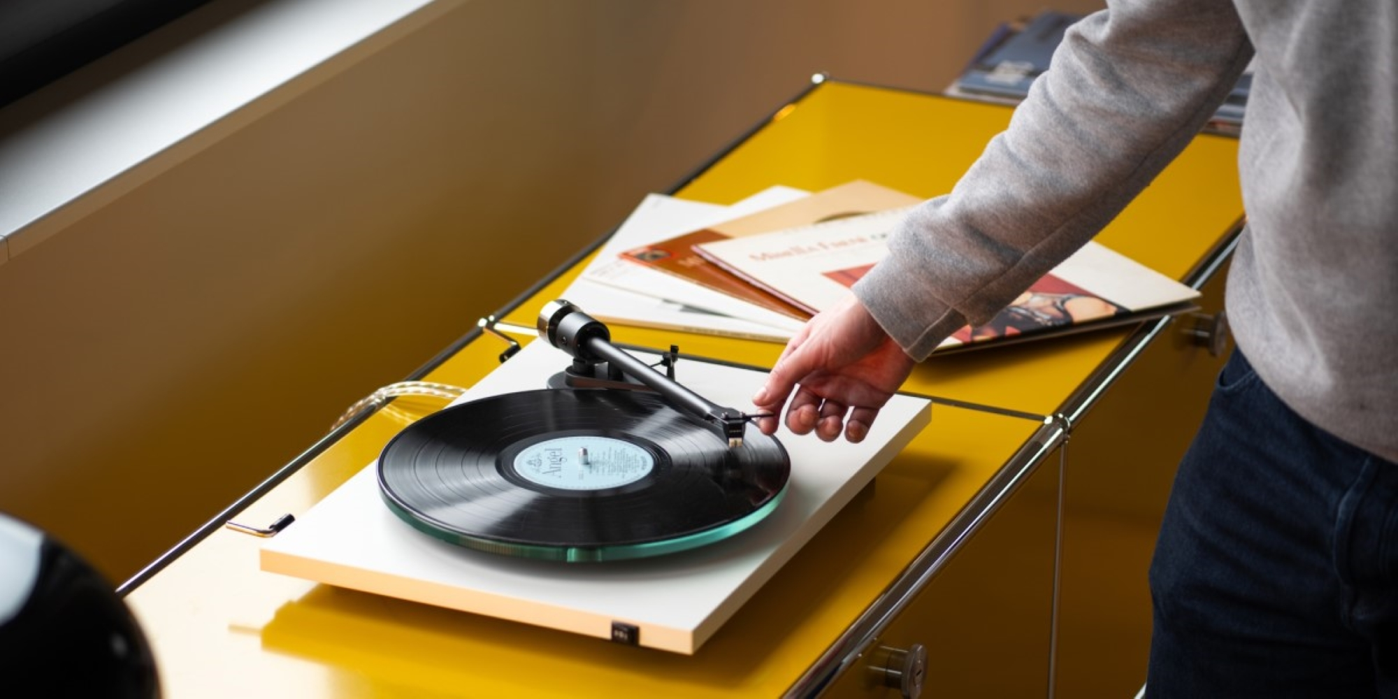 Osoba kładzie igłę na płycie na gramofonie na żółtym stole.