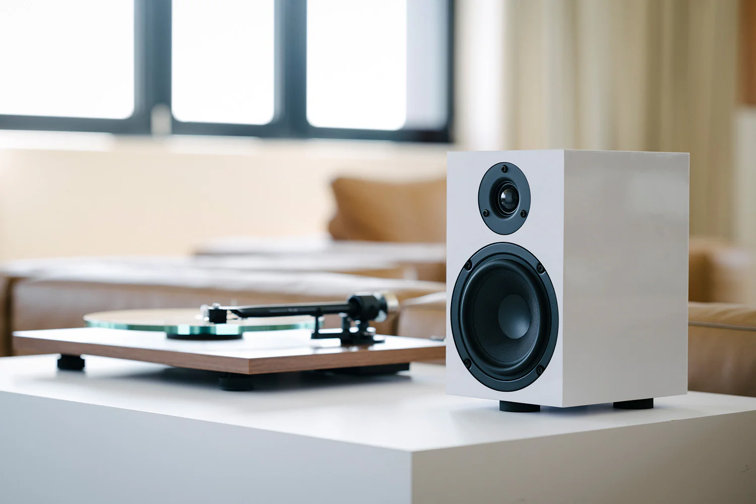 Biały głośnik i gramofon na białym stole.