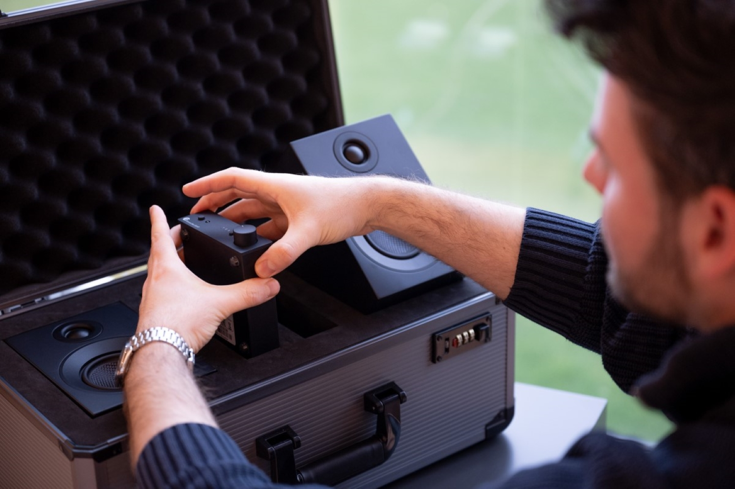 Mężczyzna wkłada czarne urządzenie audio z pokrętłem do walizki z głośnikami.