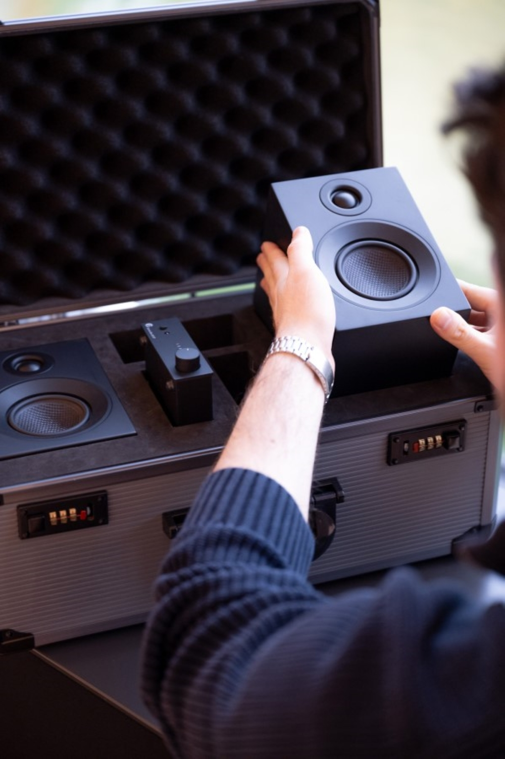 Osoba wkłada czarny głośnik do srebrnej walizki z wyściółką z pianki.