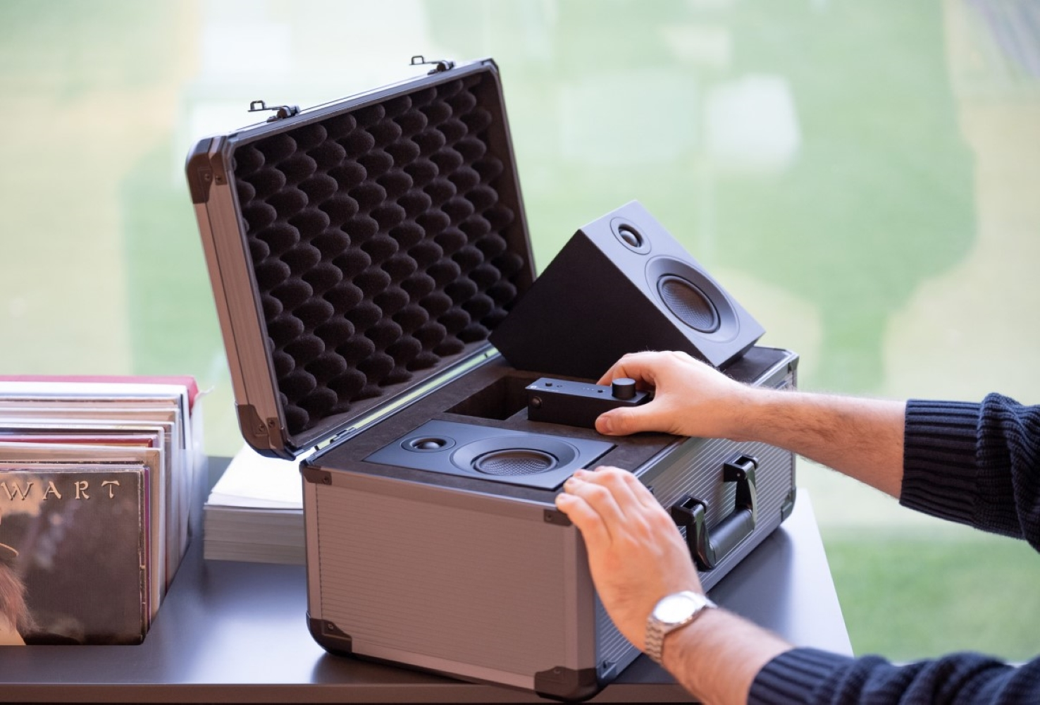 Mężczyzna rozpakowuje czarne głośniki z walizki. Stos płyt w pobliżu.