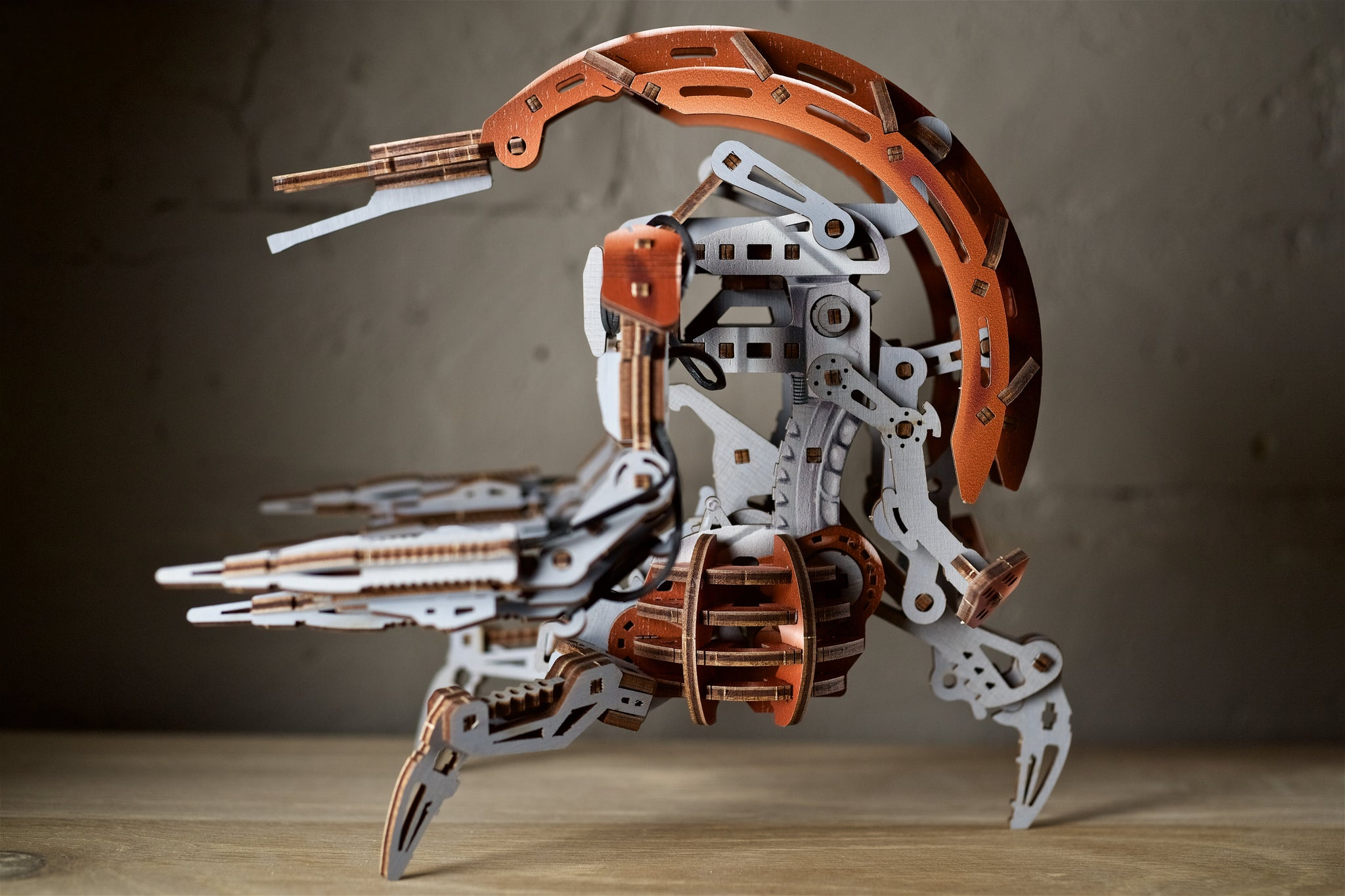 Ein hölzernes Modell eines Roboters mit Kupfer- und Grautönen auf einem Holztisch.
