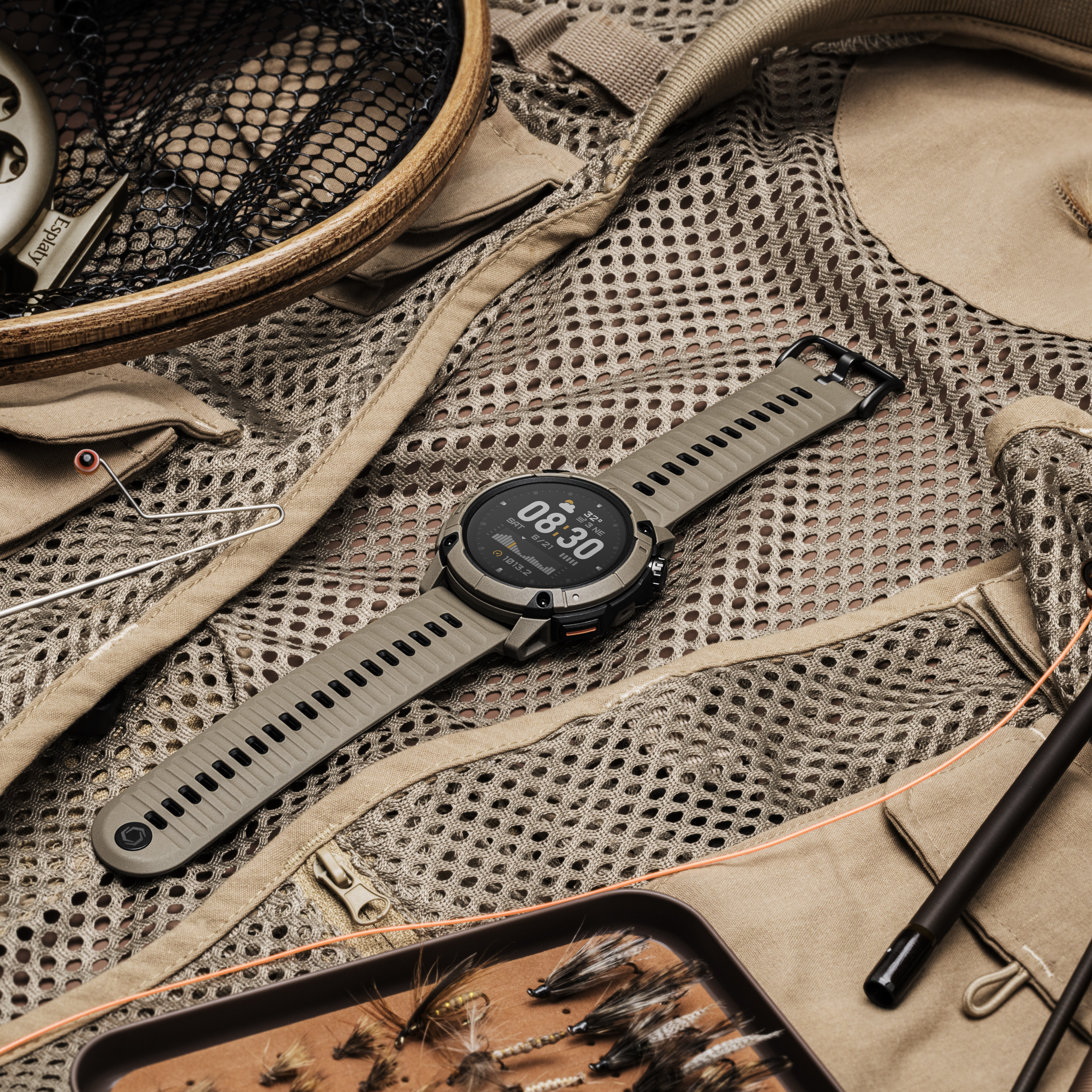 Un orologio tattico poggia su un gilet da pesca beige con mosche e rete.