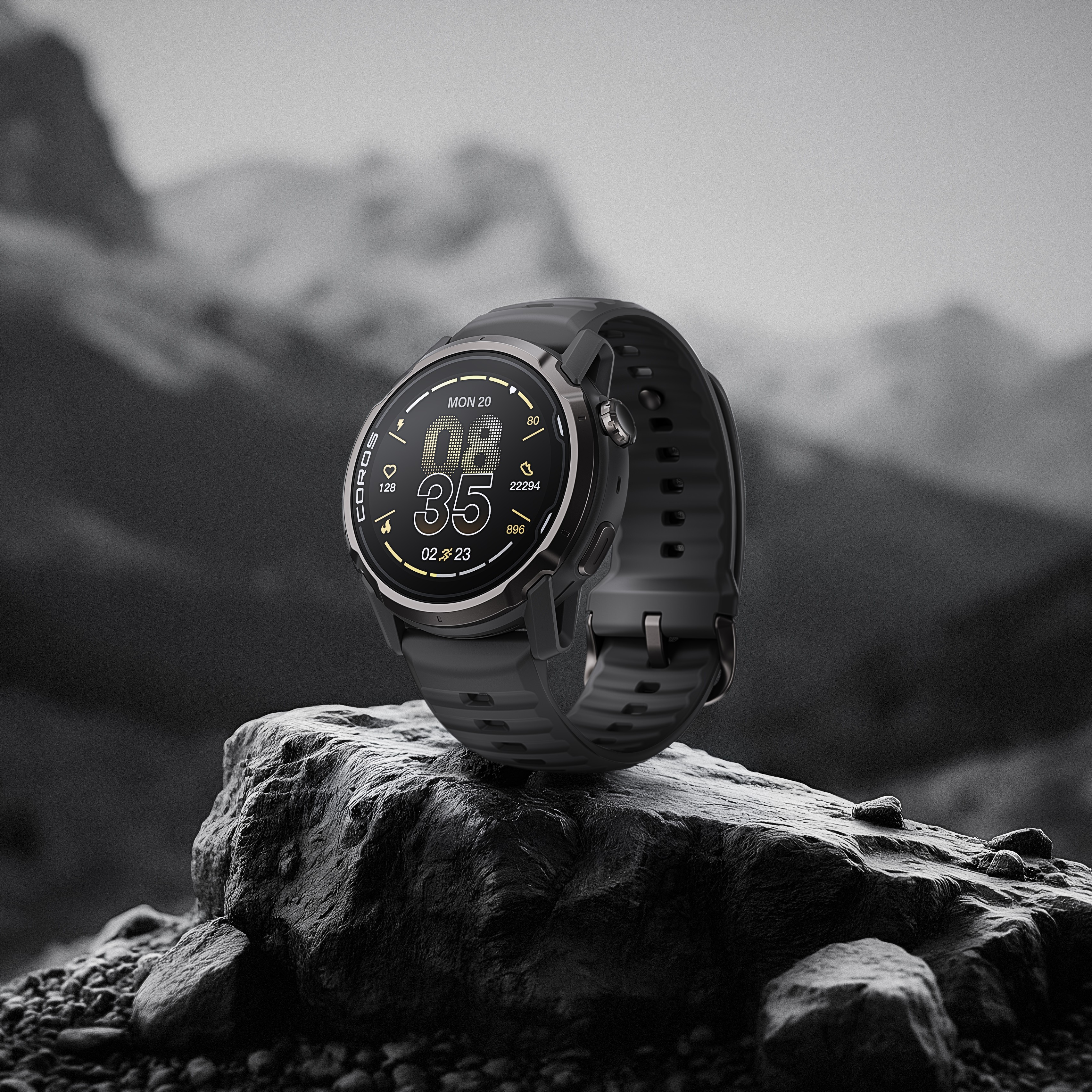Uno smartwatch scuro con display digitale riposa su una roccia, con montagne sfocate sullo sfondo.