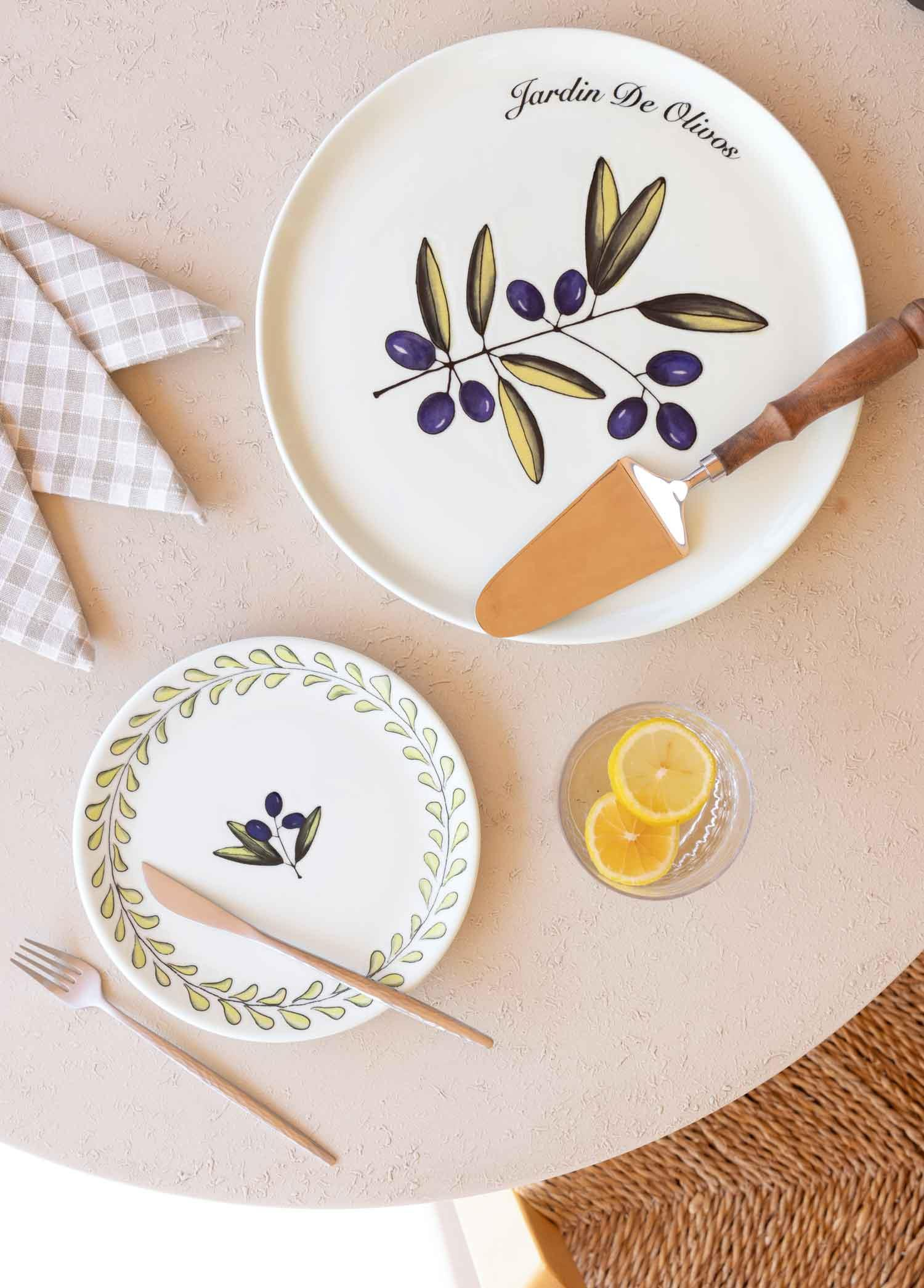İki tabak, çatal bıçak takımı, pasta servis aleti, limonlu su bardağı ve peçeteyle masa düzeni.