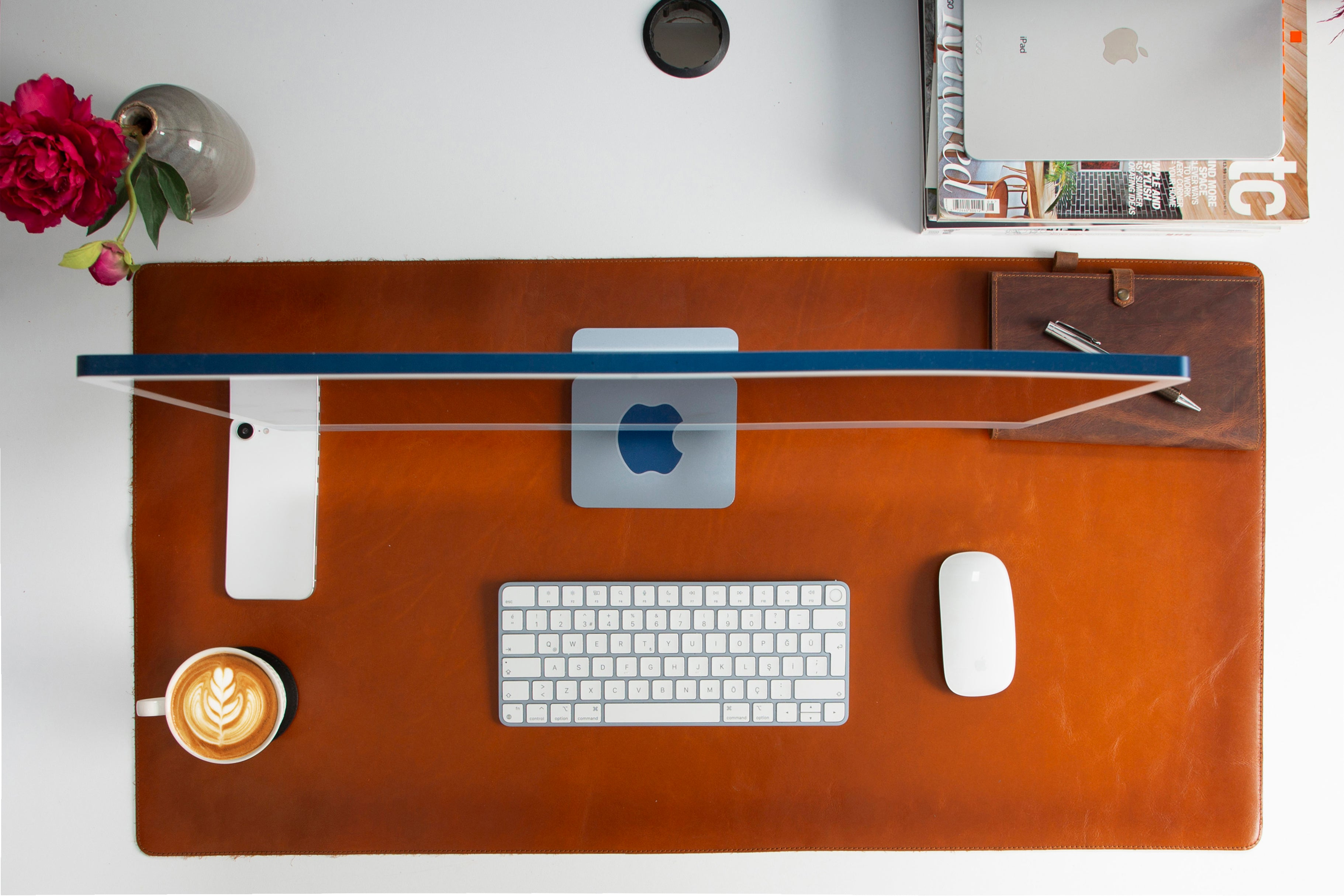 Bir iMac, klavye, fare, kahve ve çiçek içeren bir masa.