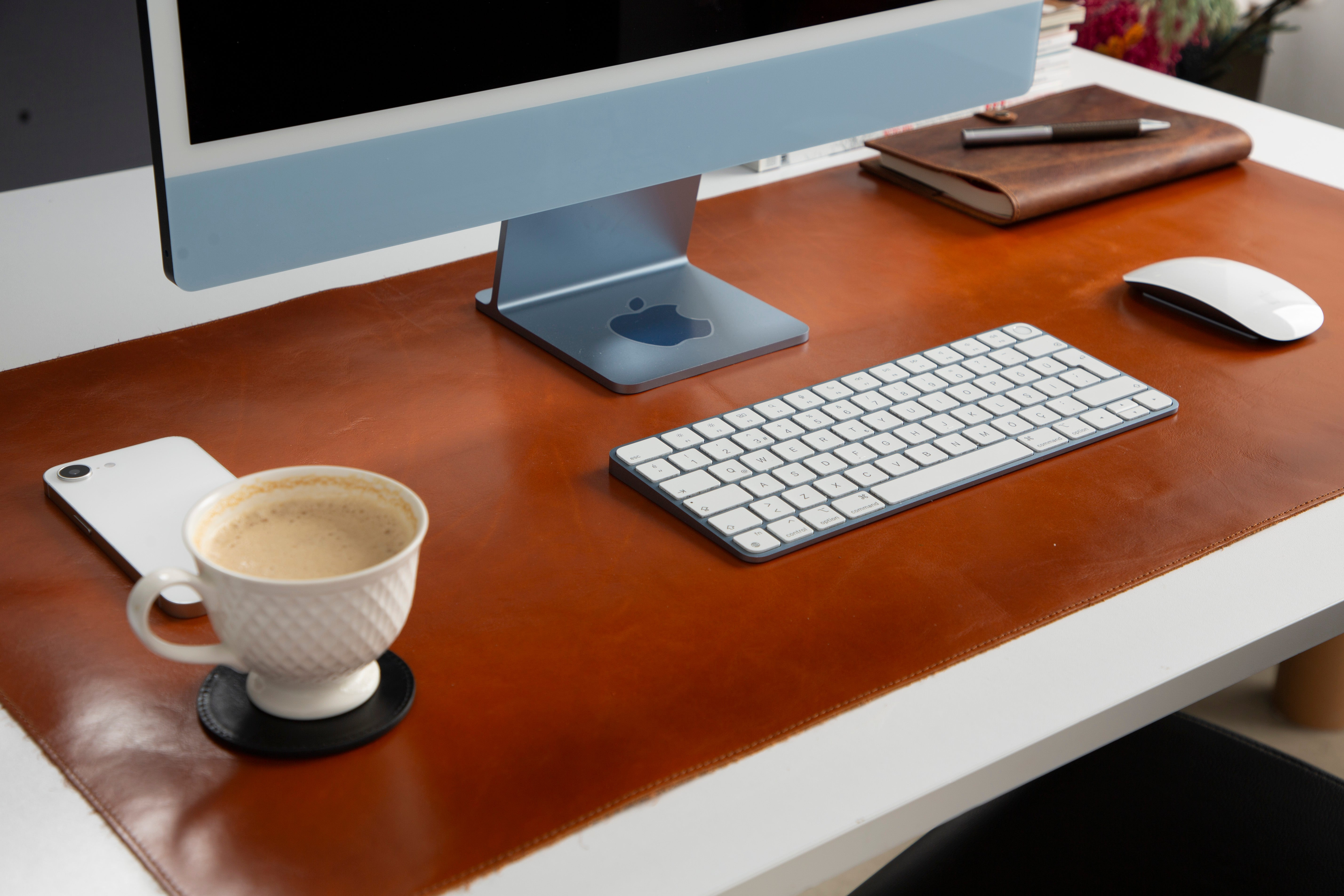 Kahverengi deri üzerinde mavi iMac, klavye, fare, akıllı telefon ve kahve.