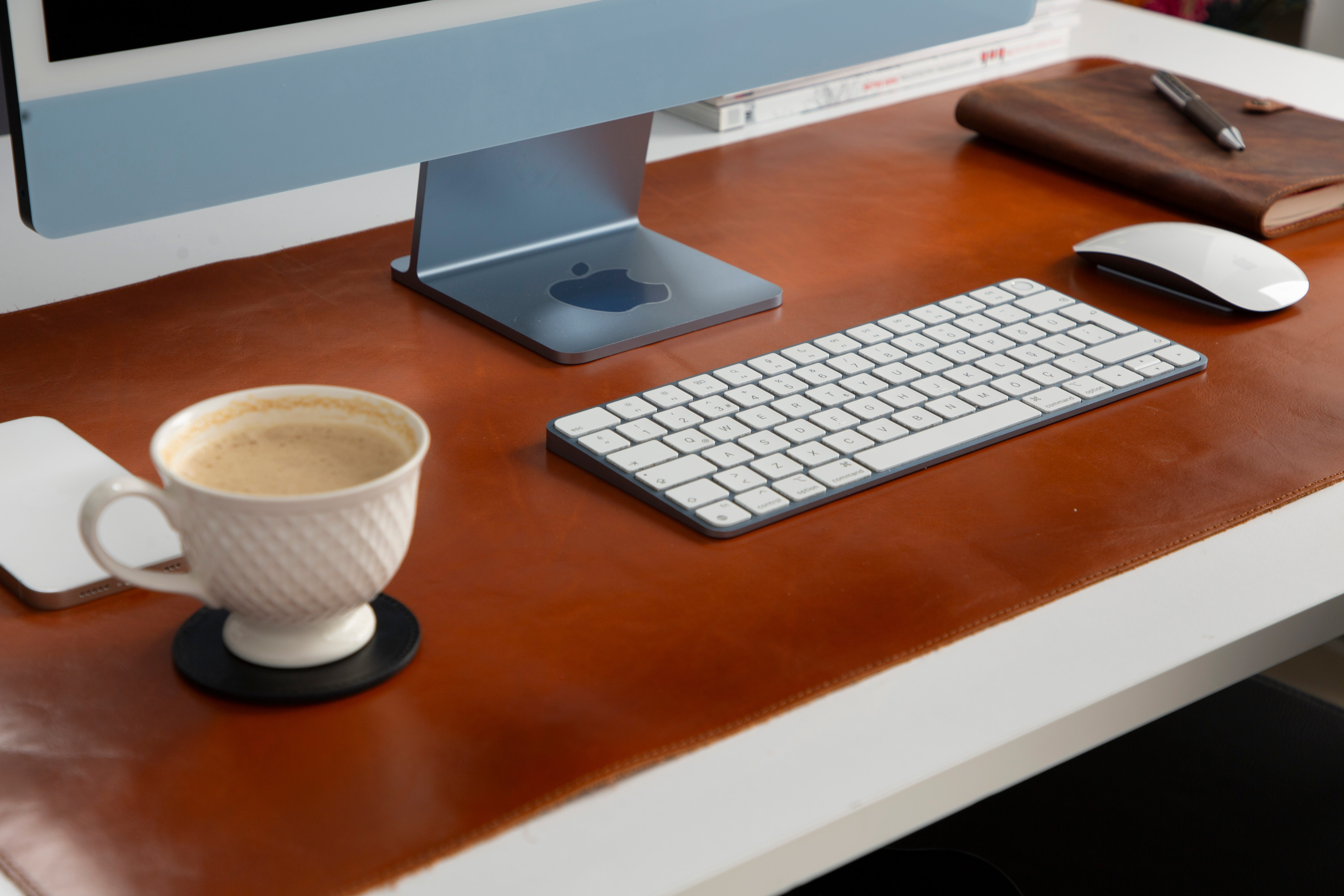 Bir iMac, klavye, fare, kahve ve defter bir masada.