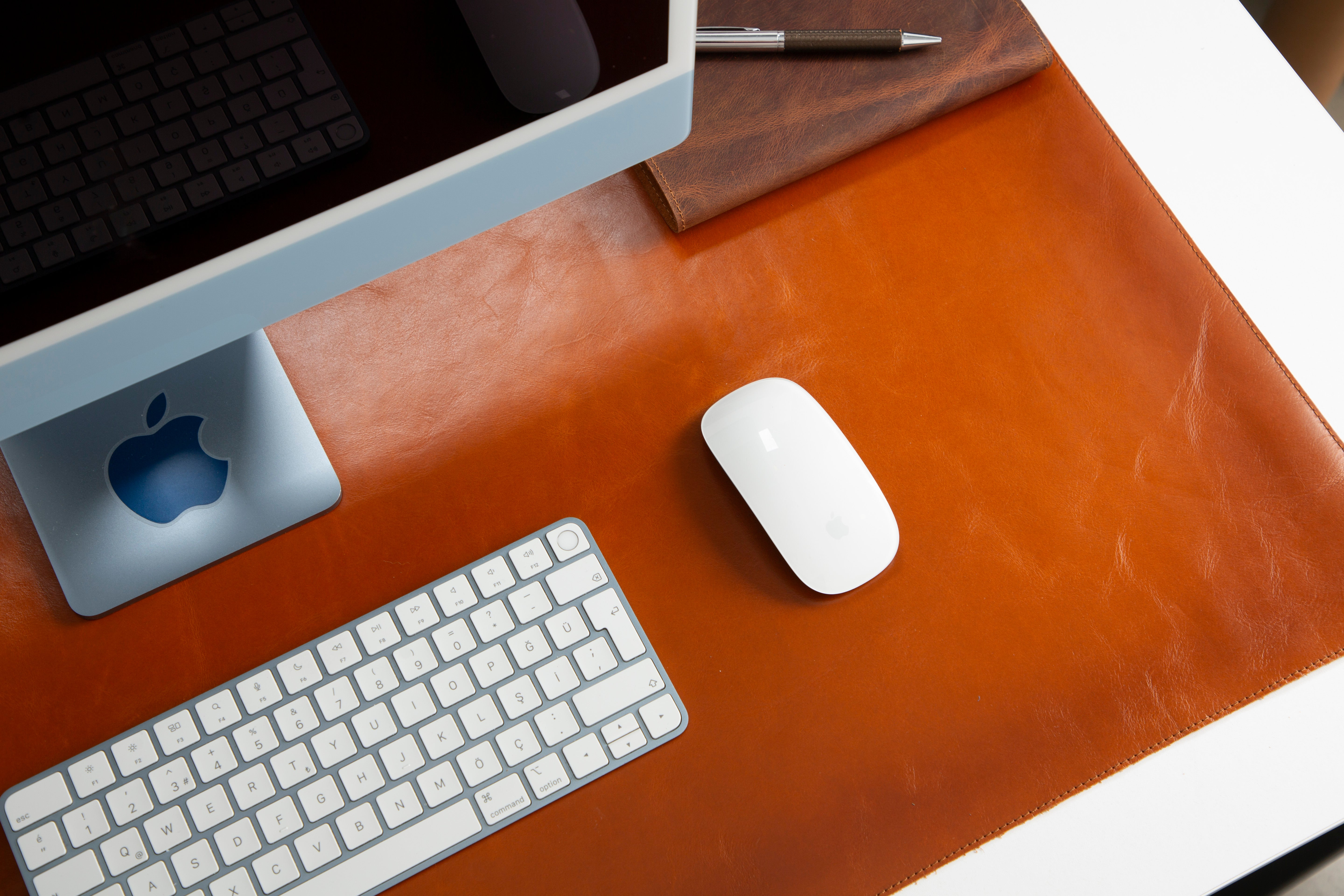 Kahverengi deri masa matı üzerinde Apple iMac, klavye, fare ve kalem duruyor.